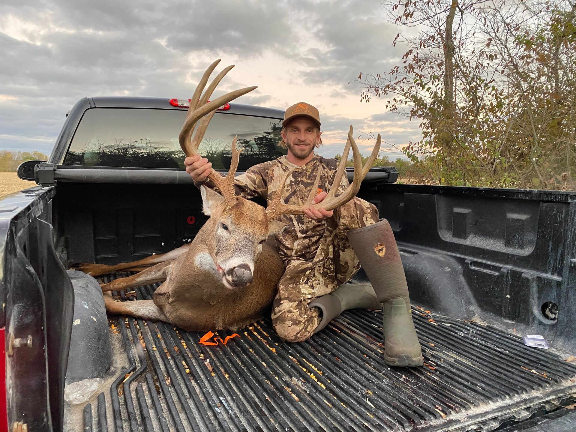 A man is sitting in the back of a truck holding a deer.