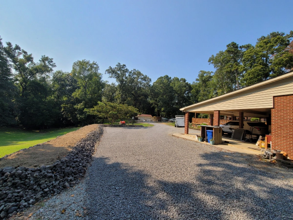 Gravel driveway leading to trees and a carport on a sunny day.