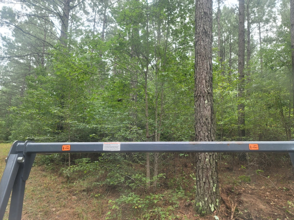 View from inside a vehicle with trees and greenery in the background and a horizontal bar in the foreground.