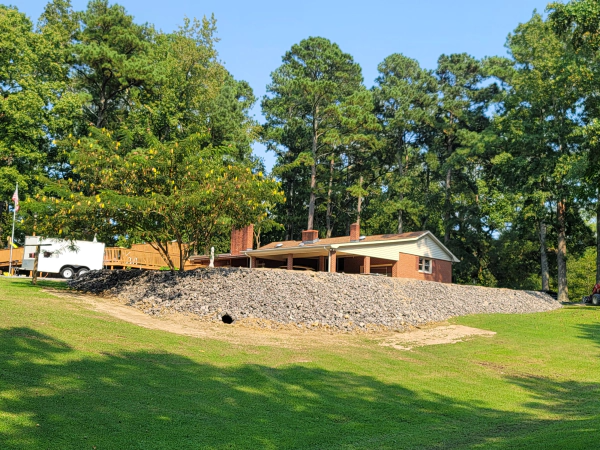 A single-story brick house with a sloping rock retaining wall on a grassy hill.