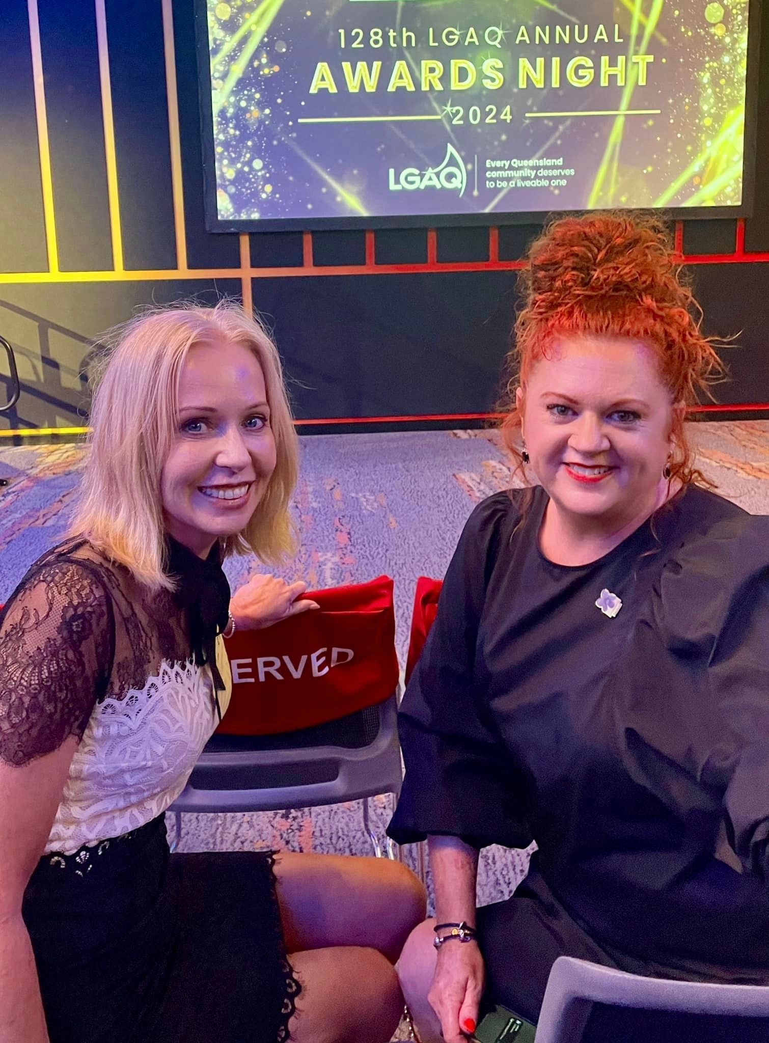 Two women are posing for a picture in front of a screen that says awards night.