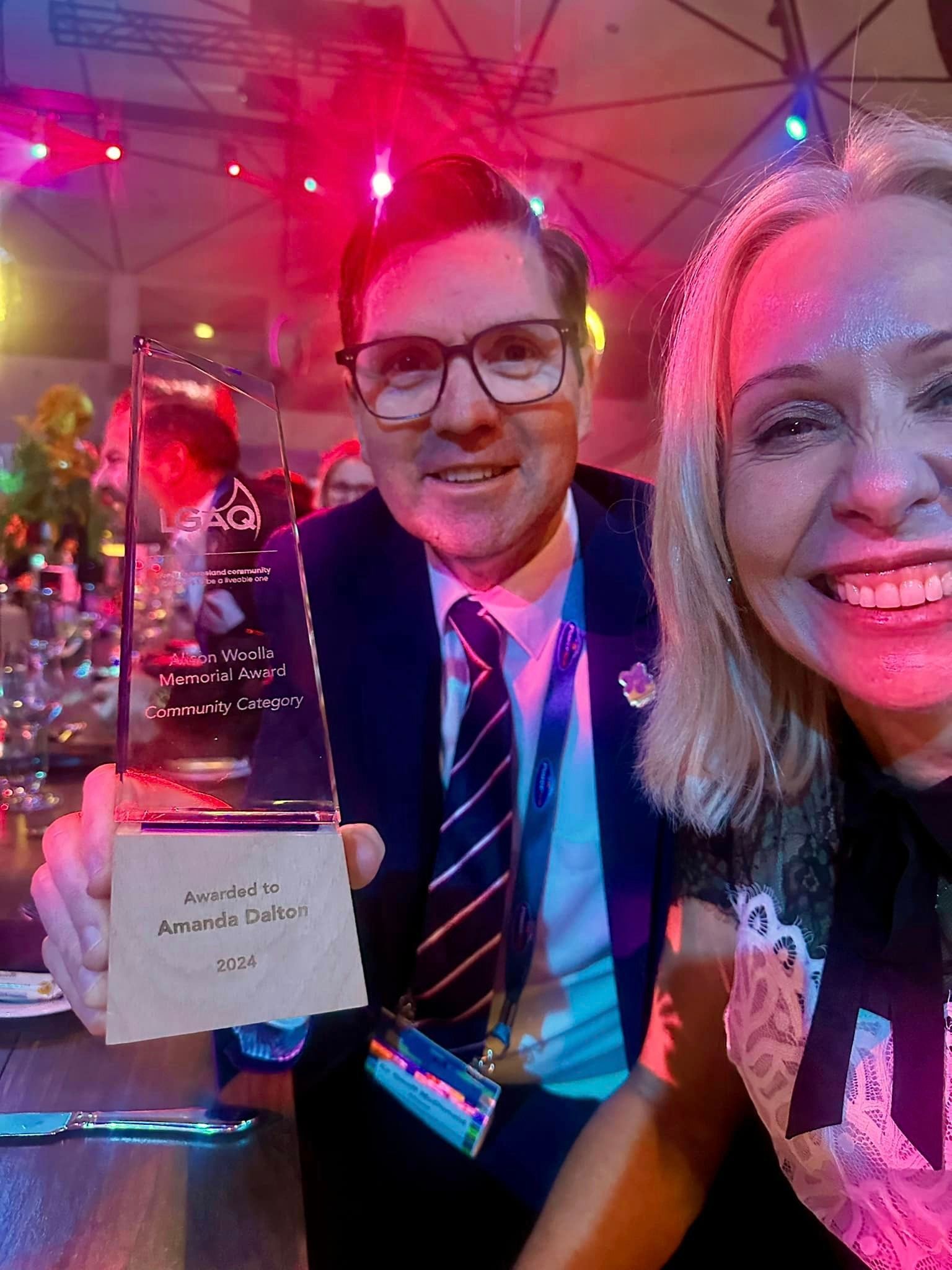 A man and a woman are posing for a picture while holding a trophy.