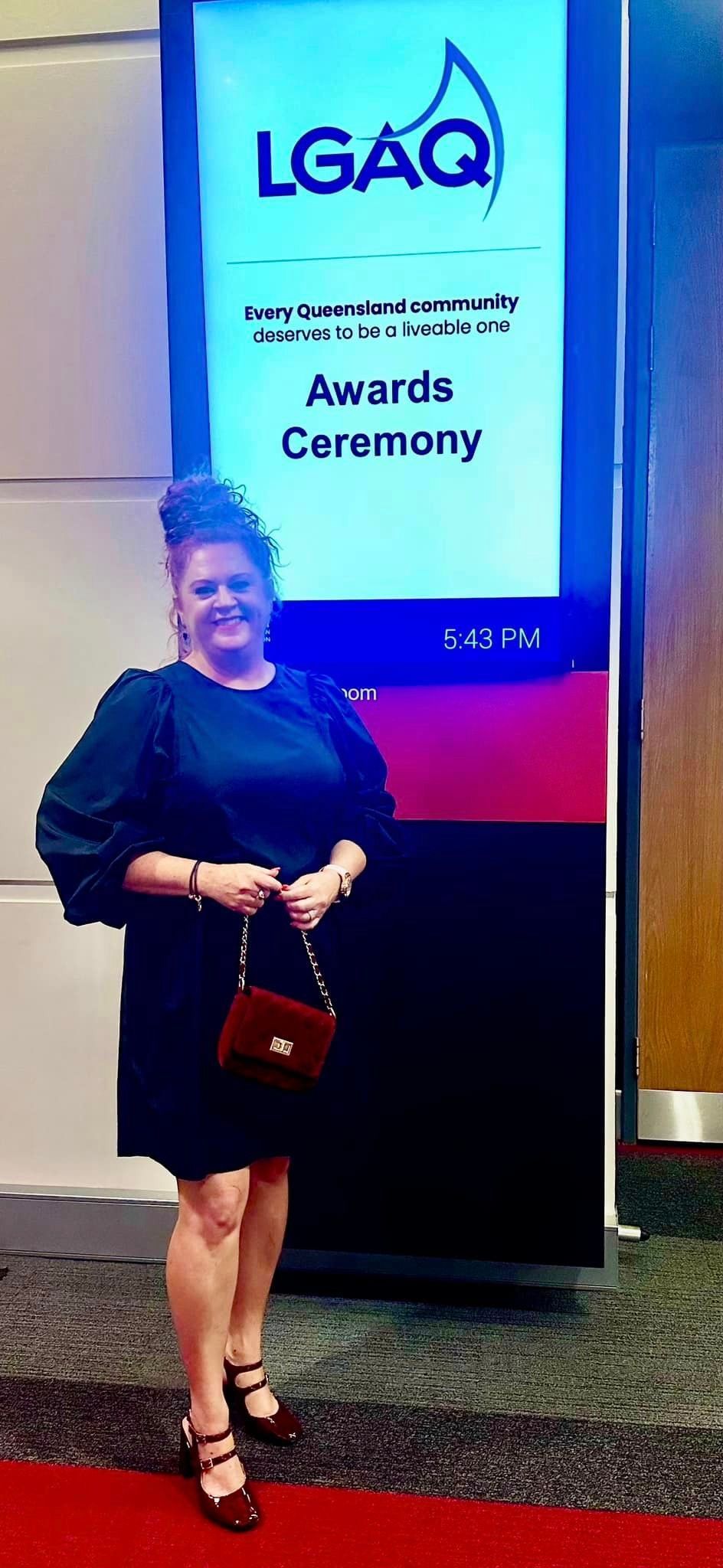 A woman in a black dress is standing in front of a large screen.