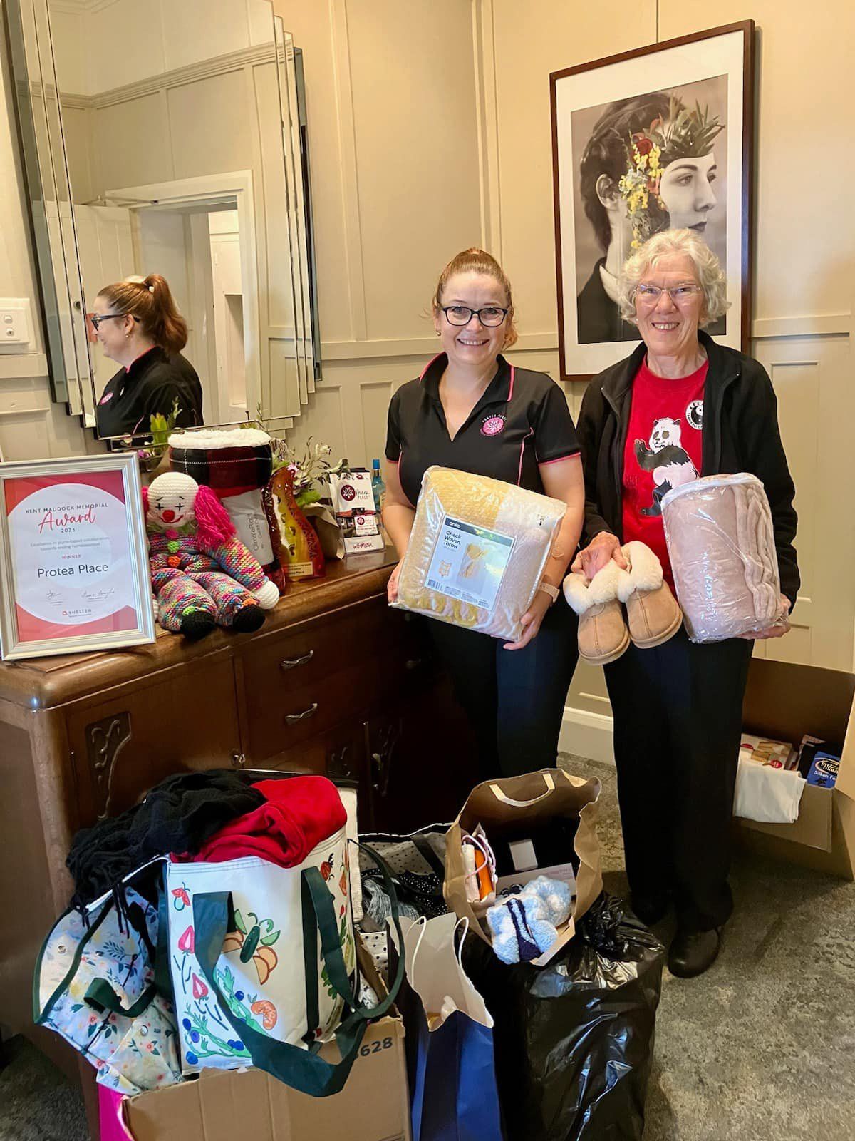 Two women are standing next to each other in a room holding boxes of donated goods.