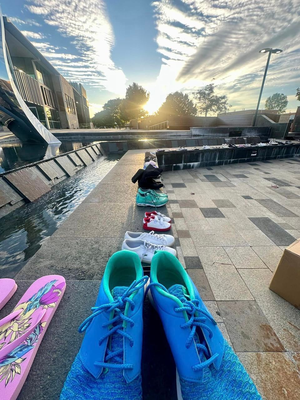 A row of shoes are lined up in front of a fountain.