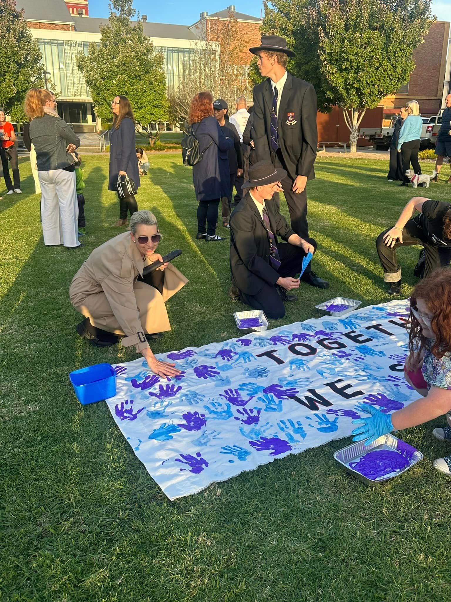 A group of people are painting a large piece of paper on the grass.