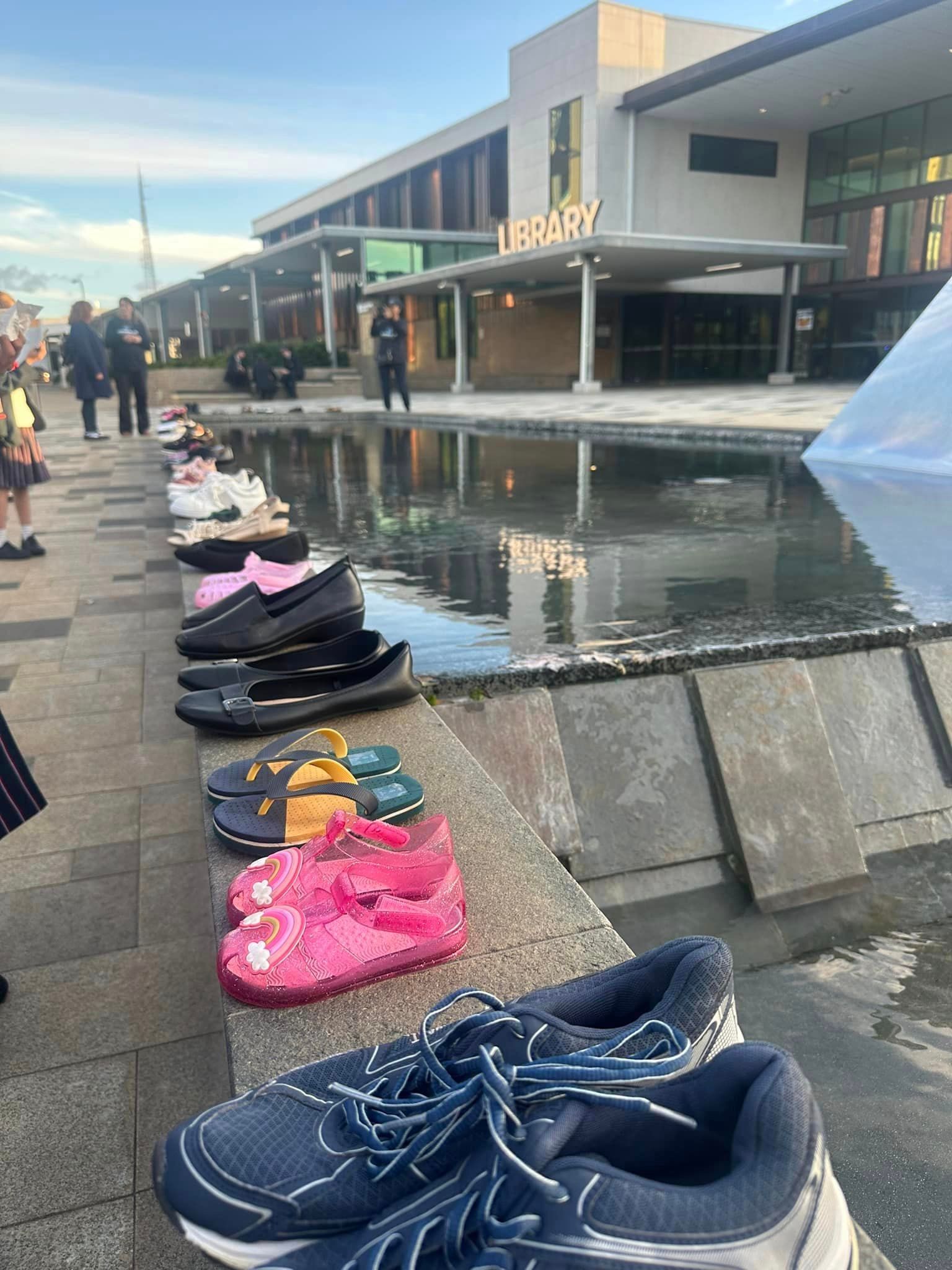 A row of shoes are lined up on a sidewalk in front of a building.