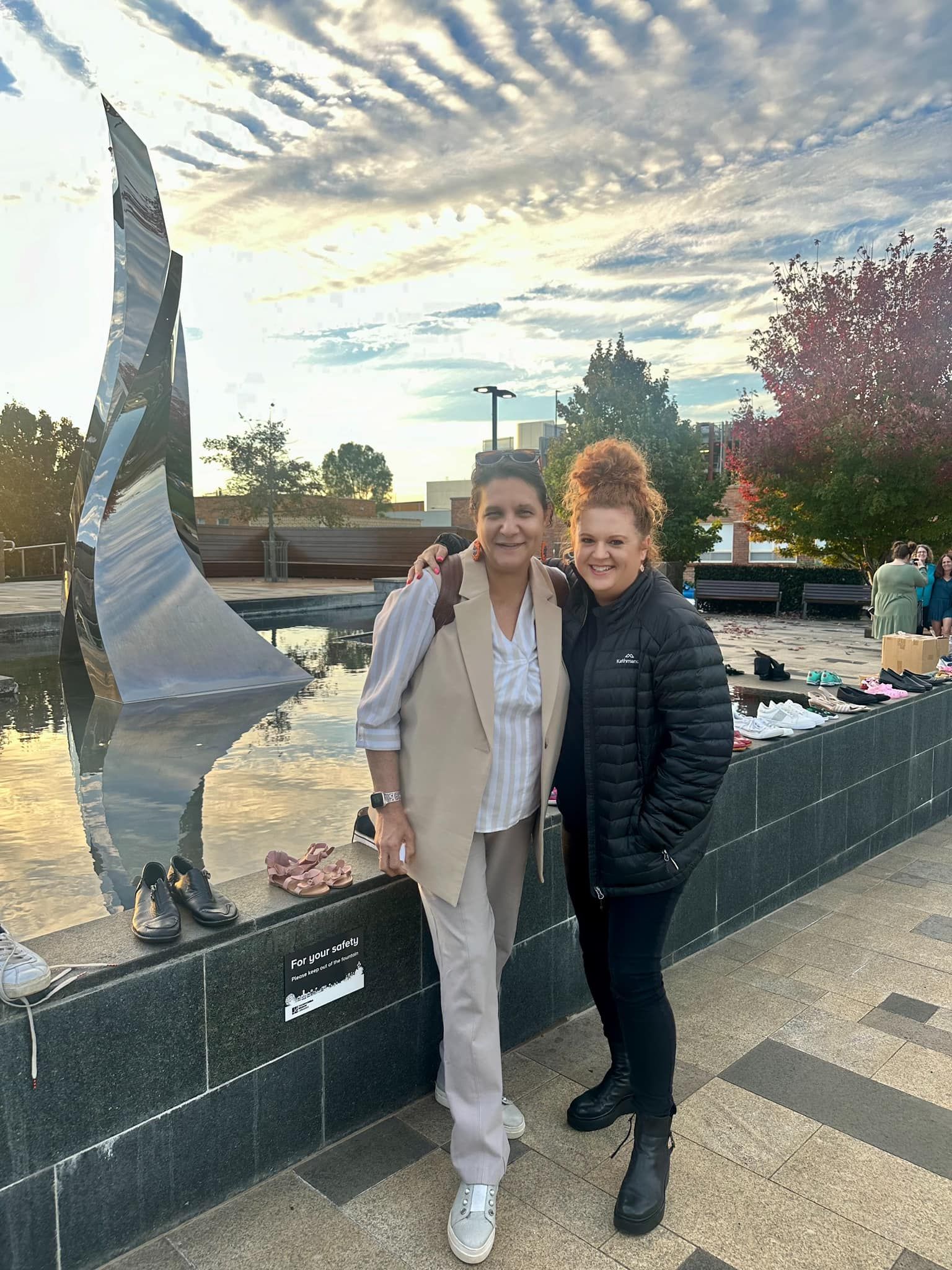 Two women are standing next to each other in front of a sculpture.