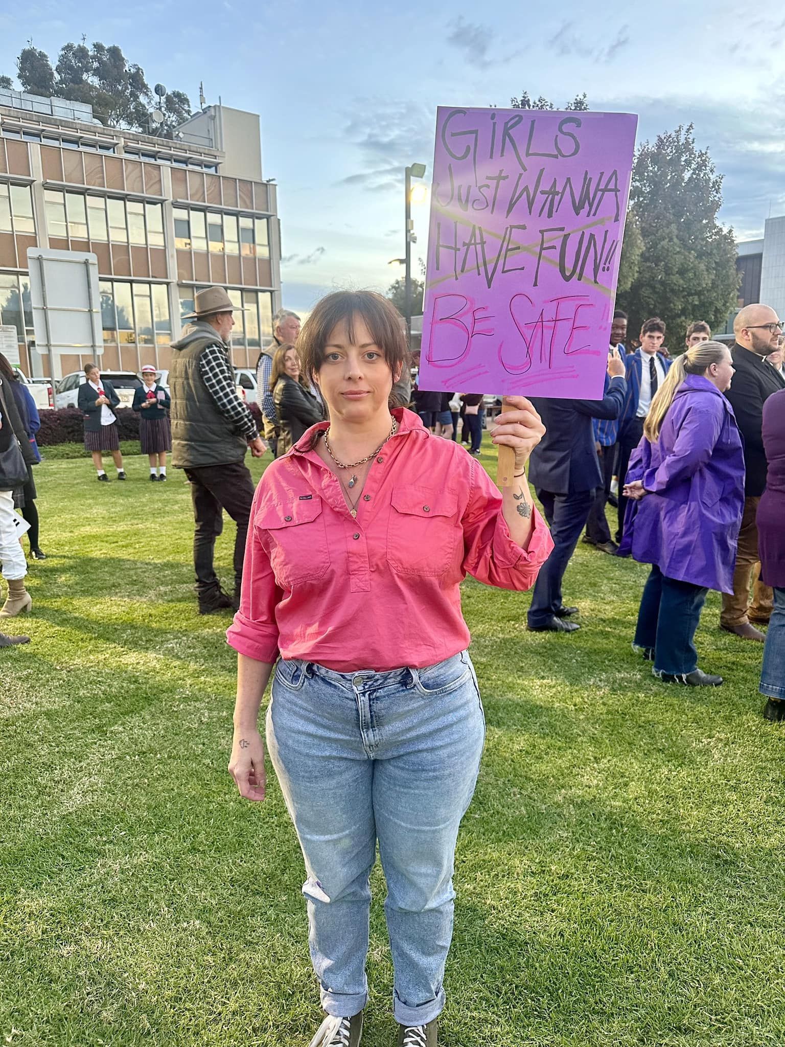 A woman in a pink shirt is holding a purple sign.