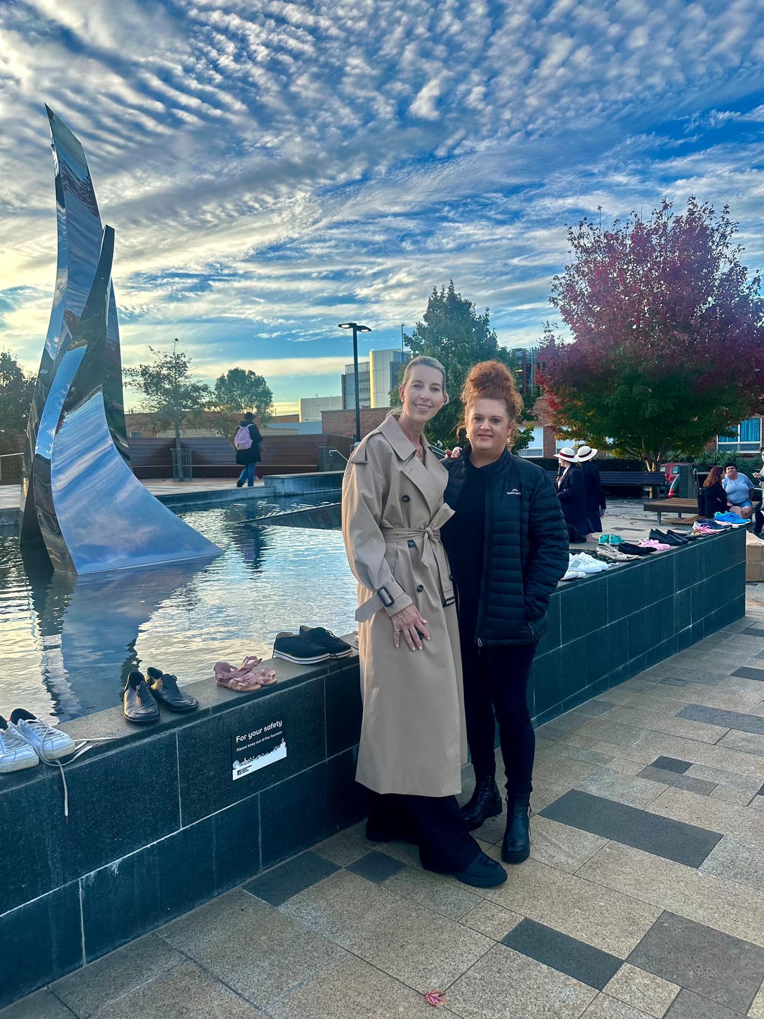 Two women are standing next to each other in front of a fountain.