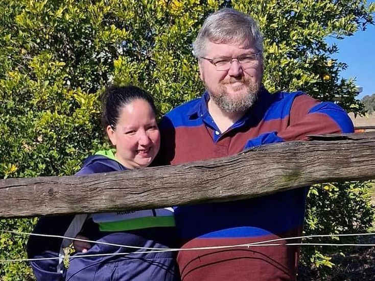 A man and a woman are standing next to a wooden fence.