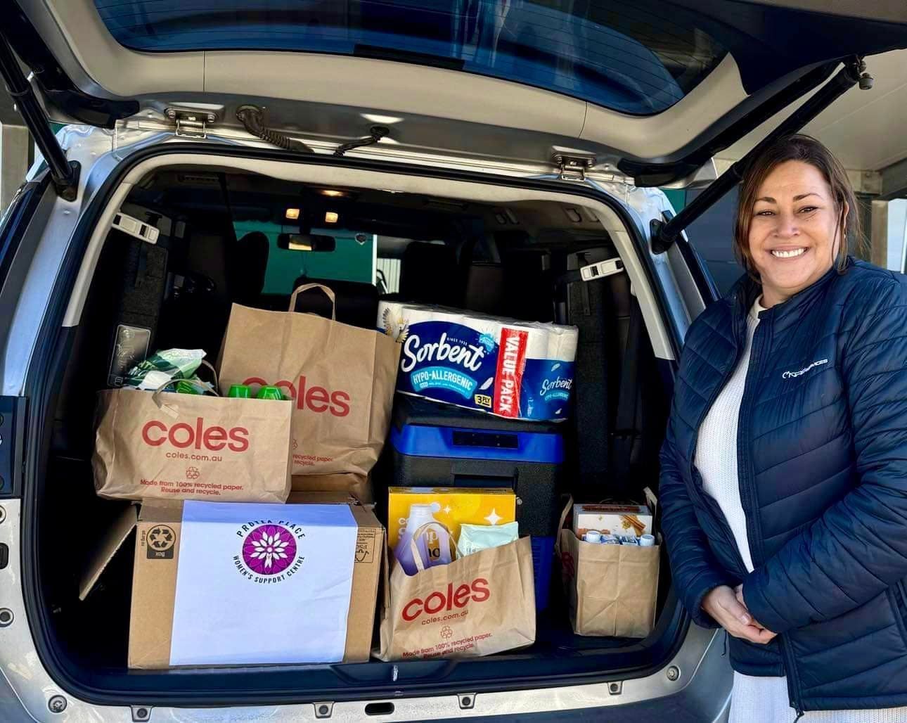 A woman is standing in front of a car filled with shopping bags.