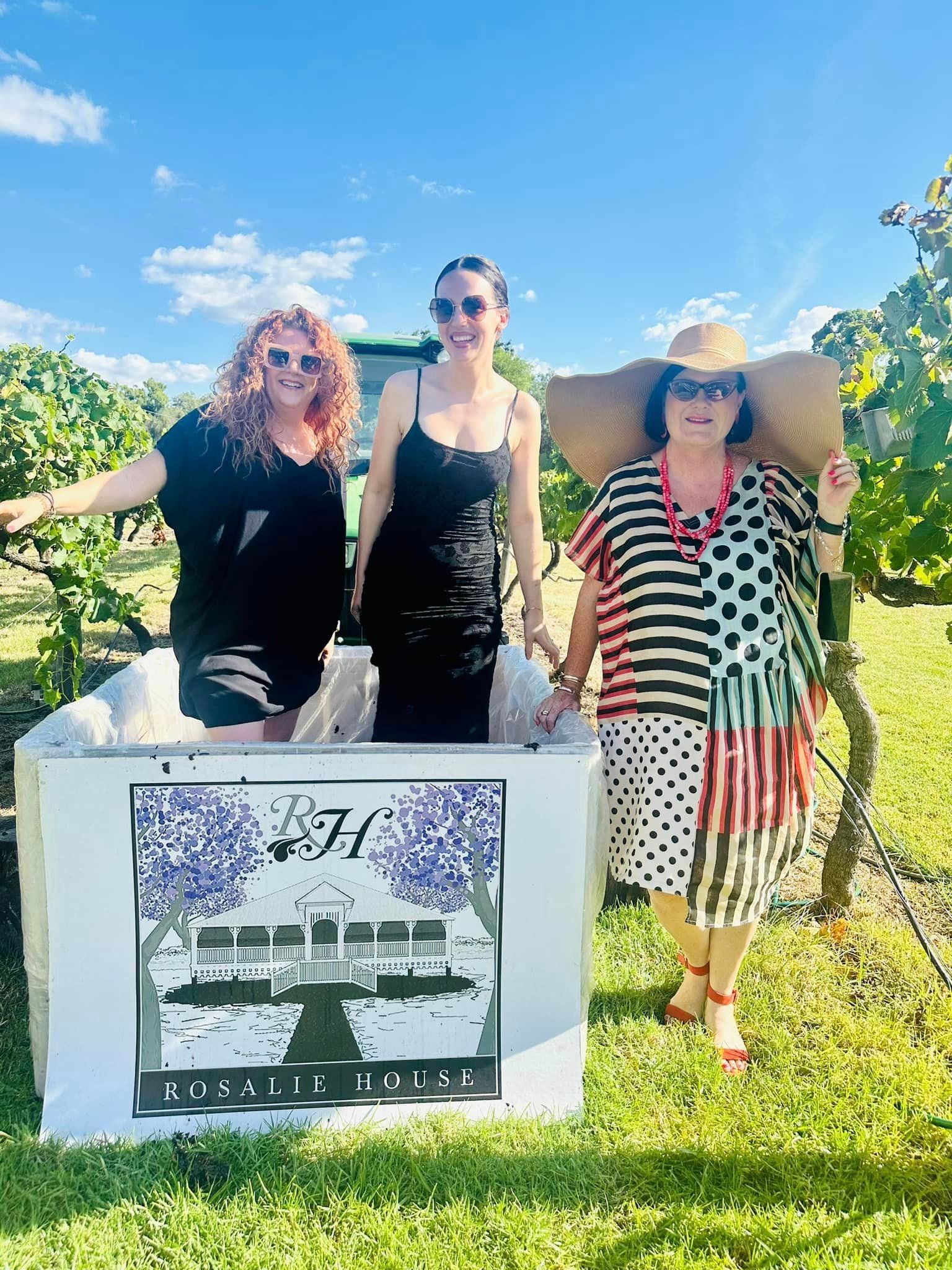 Three women are standing next to each other in a field holding a sign.