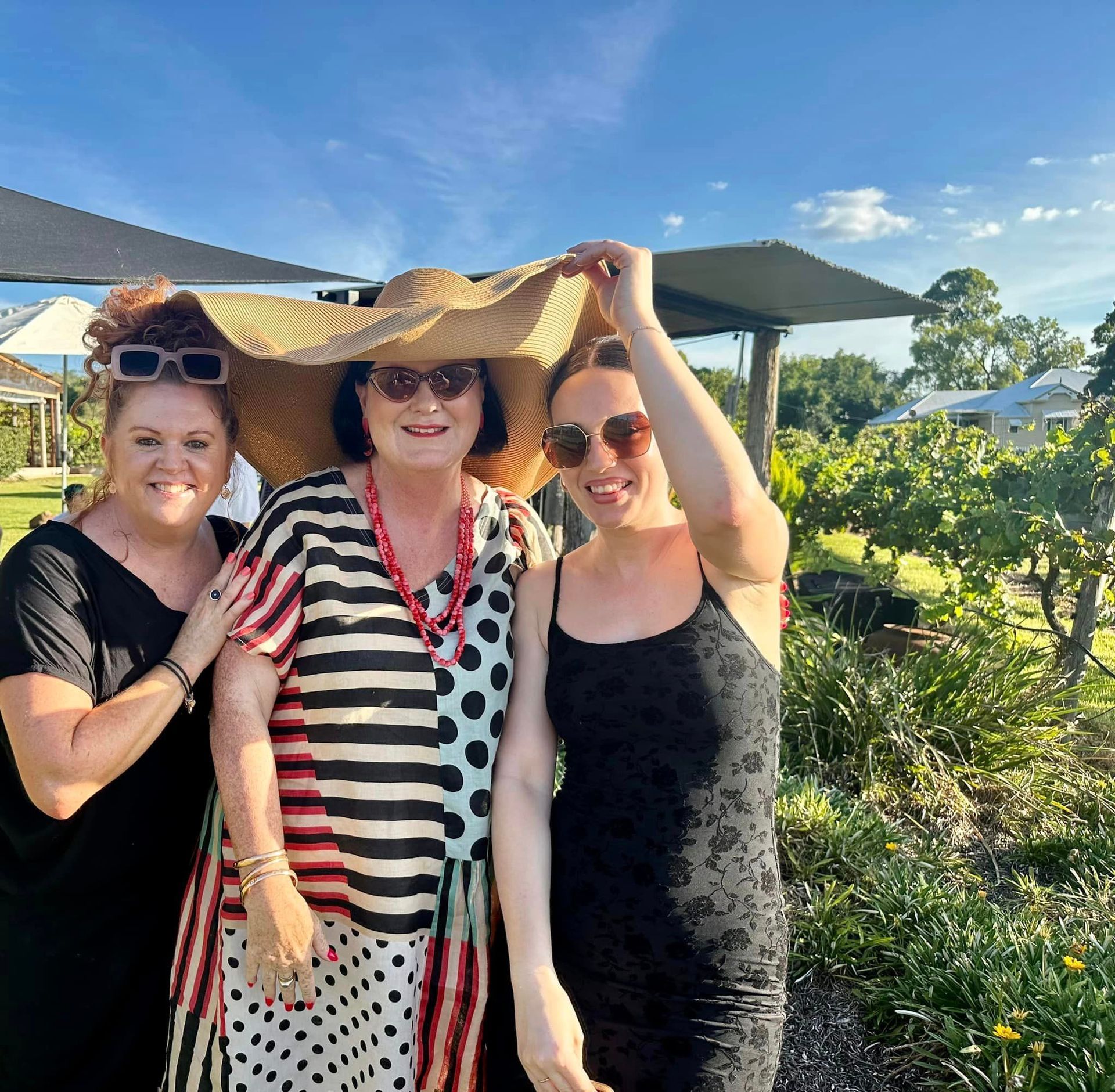 Three women are posing for a picture with one wearing a straw hat