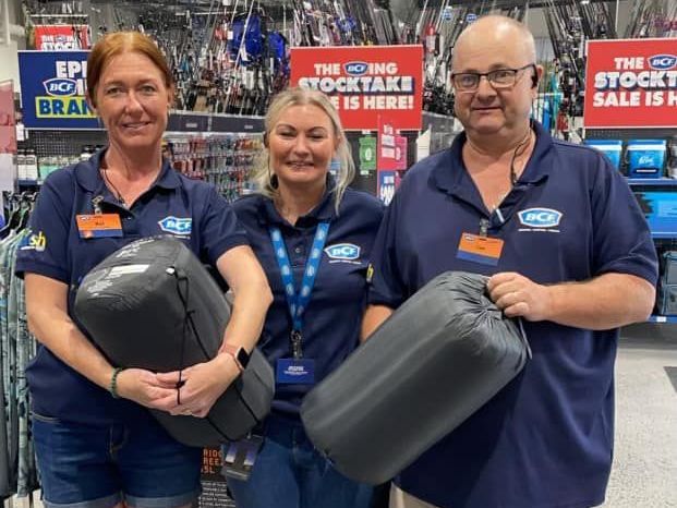 A man and two women are holding sleeping bags in a store.