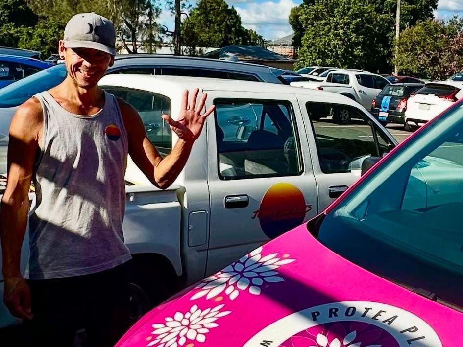 Jonny Buckets is standing next to a pink Protea Place car.