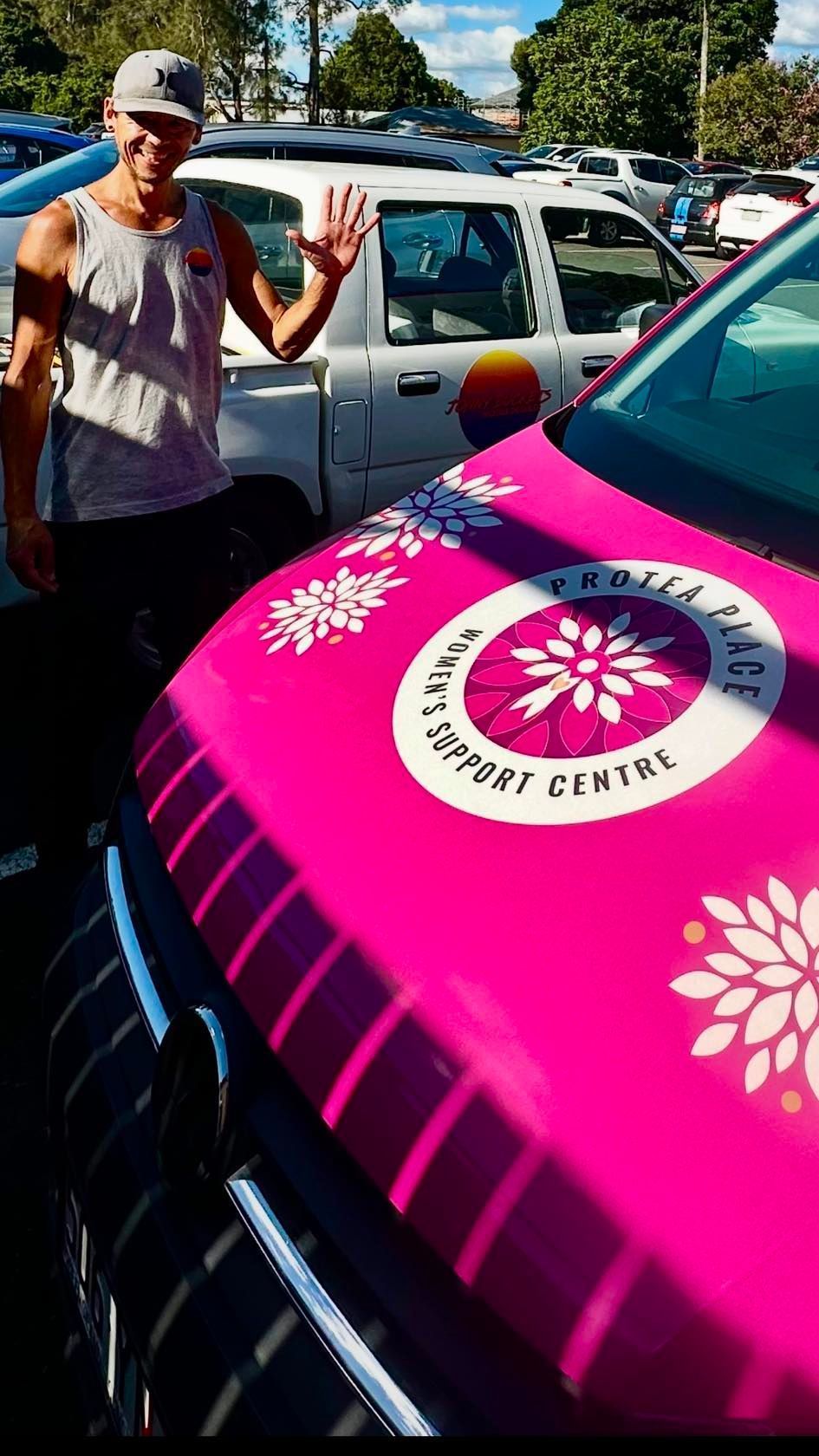 Jonny Buckets is standing next to a pink Protea Place car.