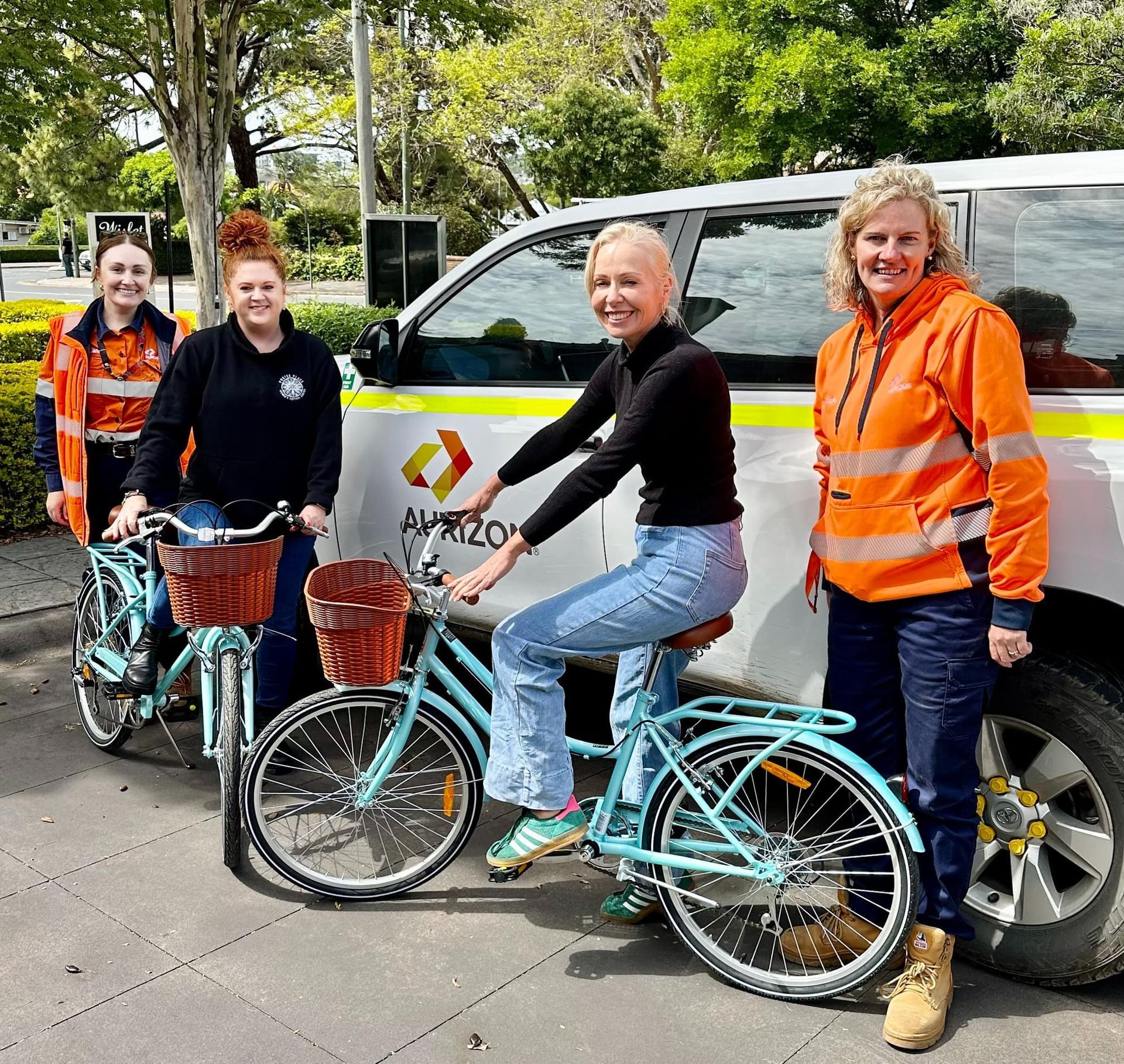 A group of women are standing next to bicycles in front of a van.