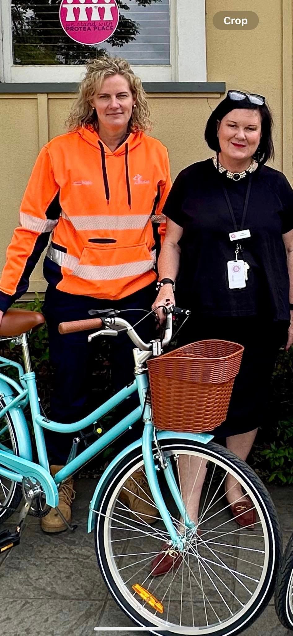 Two women are standing next to each other next to a bicycle.