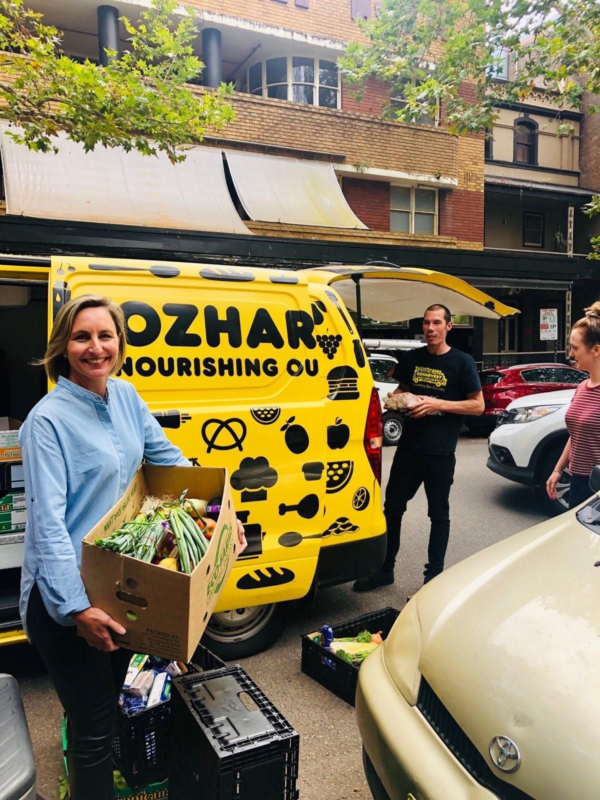 A woman is holding a box of food in front of a yellow van.
