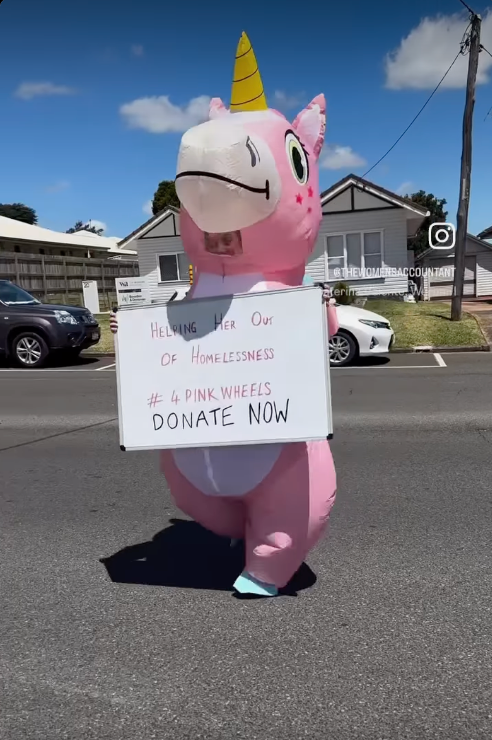 A pink inflatable unicorn is holding a sign that says donate now.