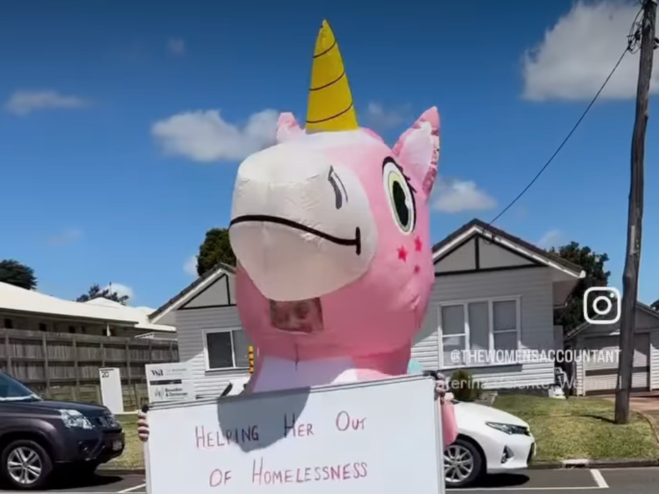 A pink inflatable unicorn is holding a sign that says donate now.