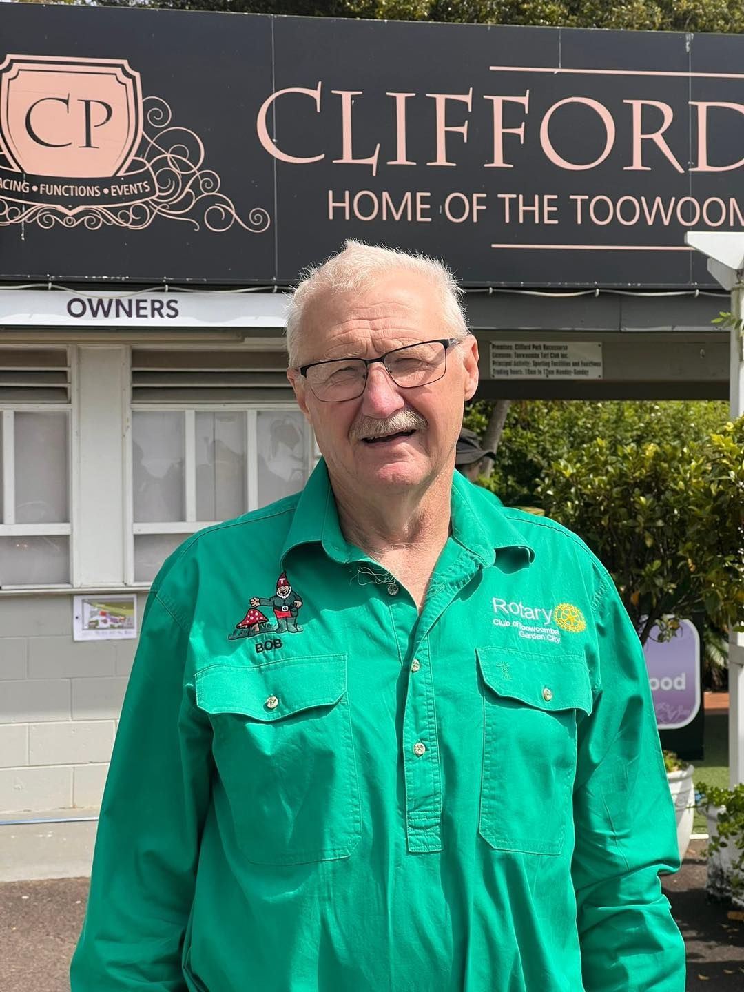 A man in a green shirt is standing in front of a sign for Clifford Park Racecourse