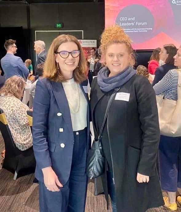 Two women are posing for a picture together at a conference.