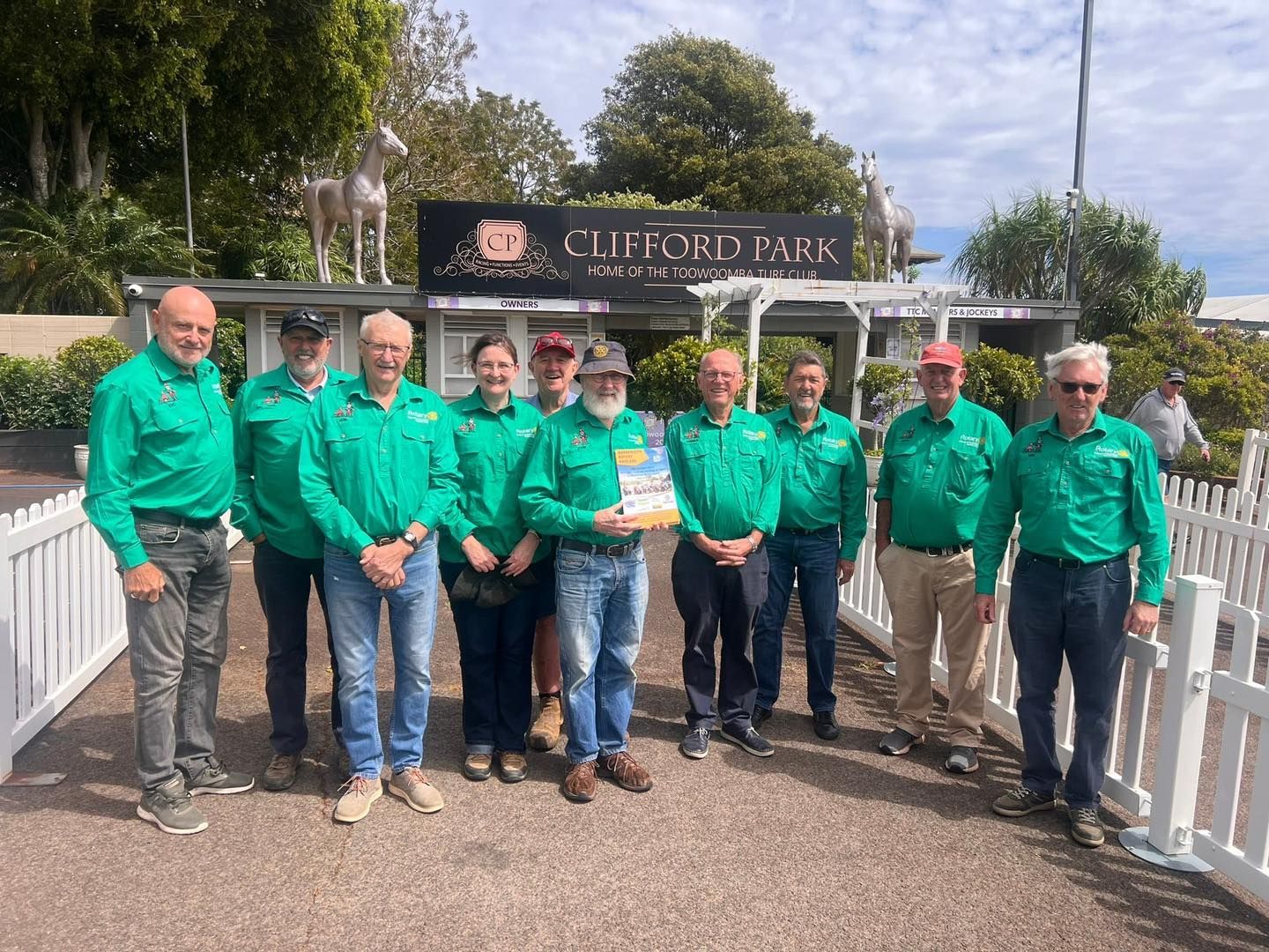 A group of men in green shirts are standing in front of a sign for clifford park.