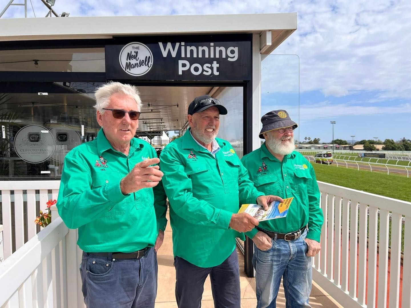 Three men are standing in front of a winning post sign.