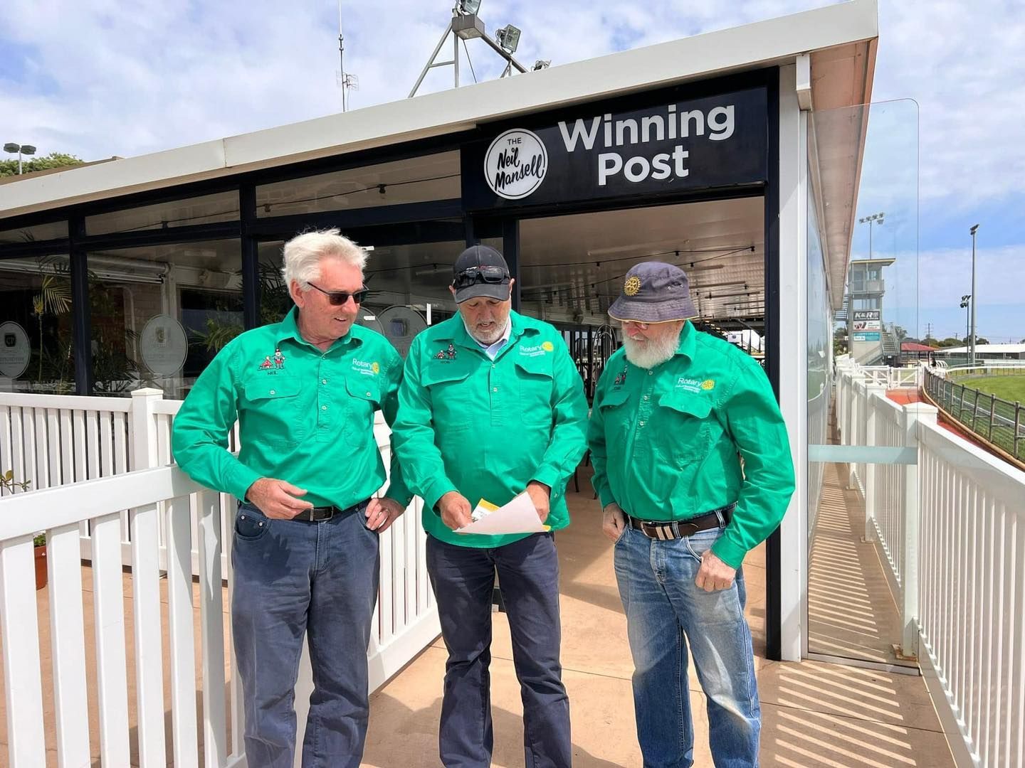 Three men are standing in front of a building that says winning post