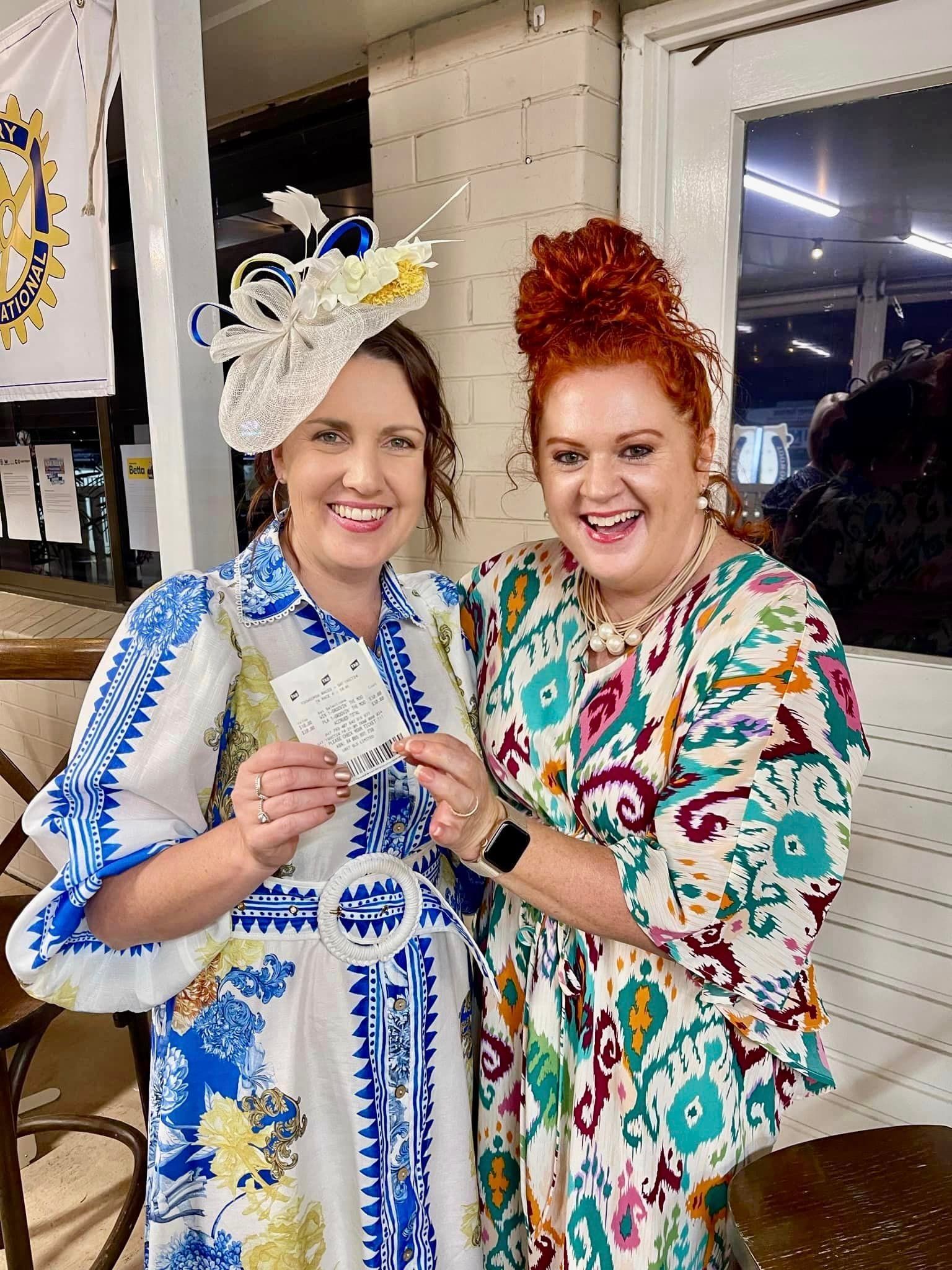 Two women are standing next to each other and smiling while holding a card.