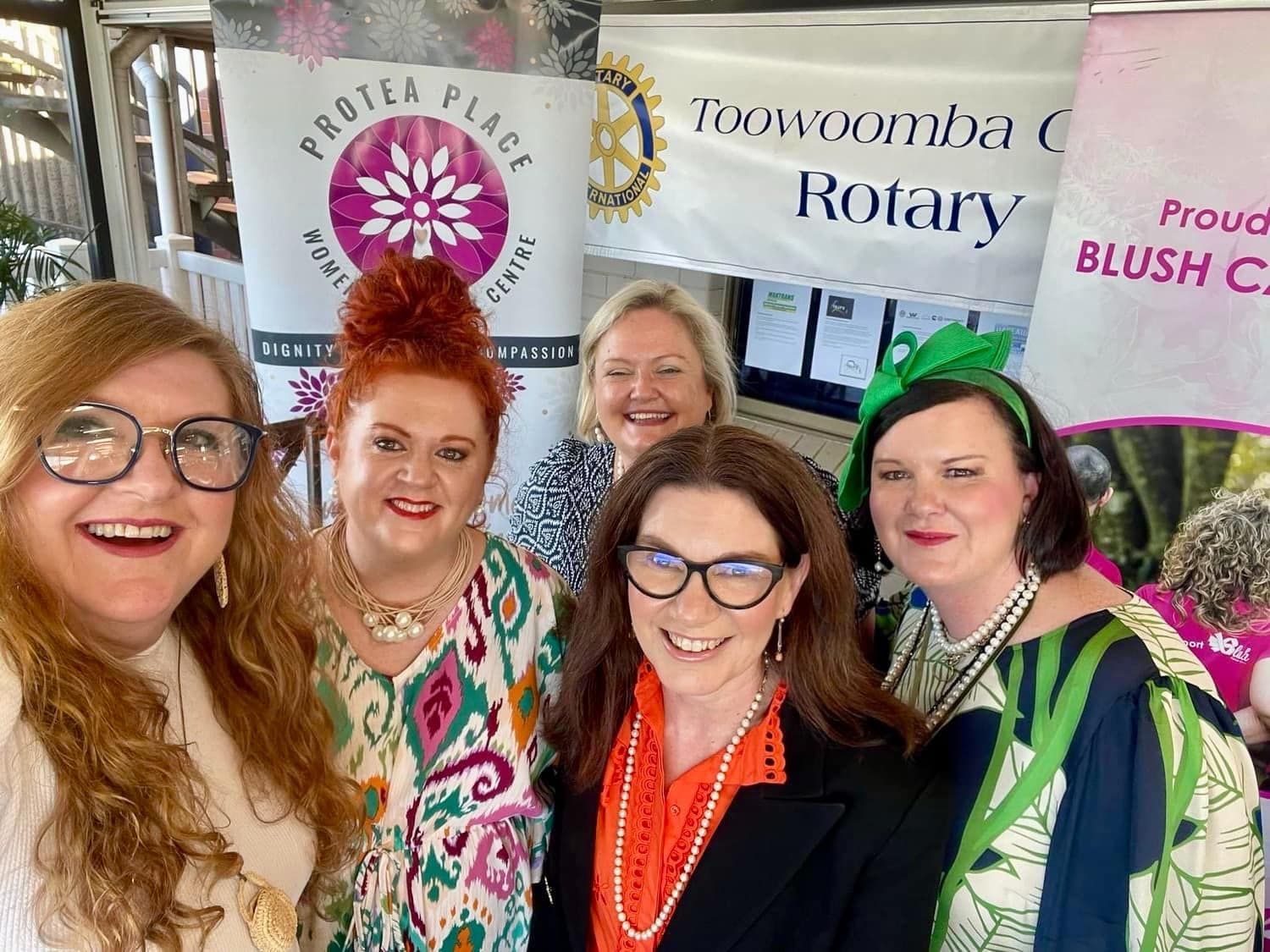 A group of women are posing for a picture in front of a rotary banner.