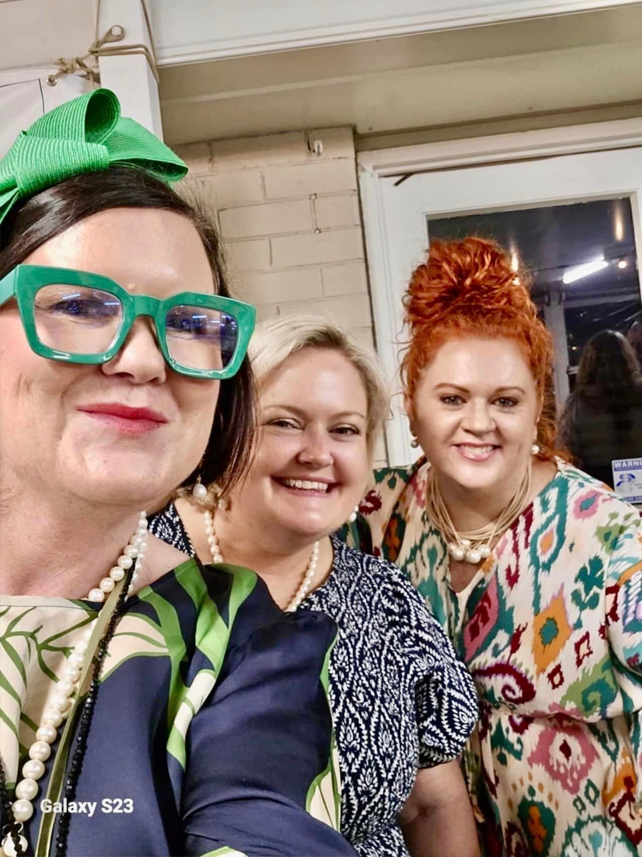 Three women are posing for a picture together and one of them is wearing green glasses.
