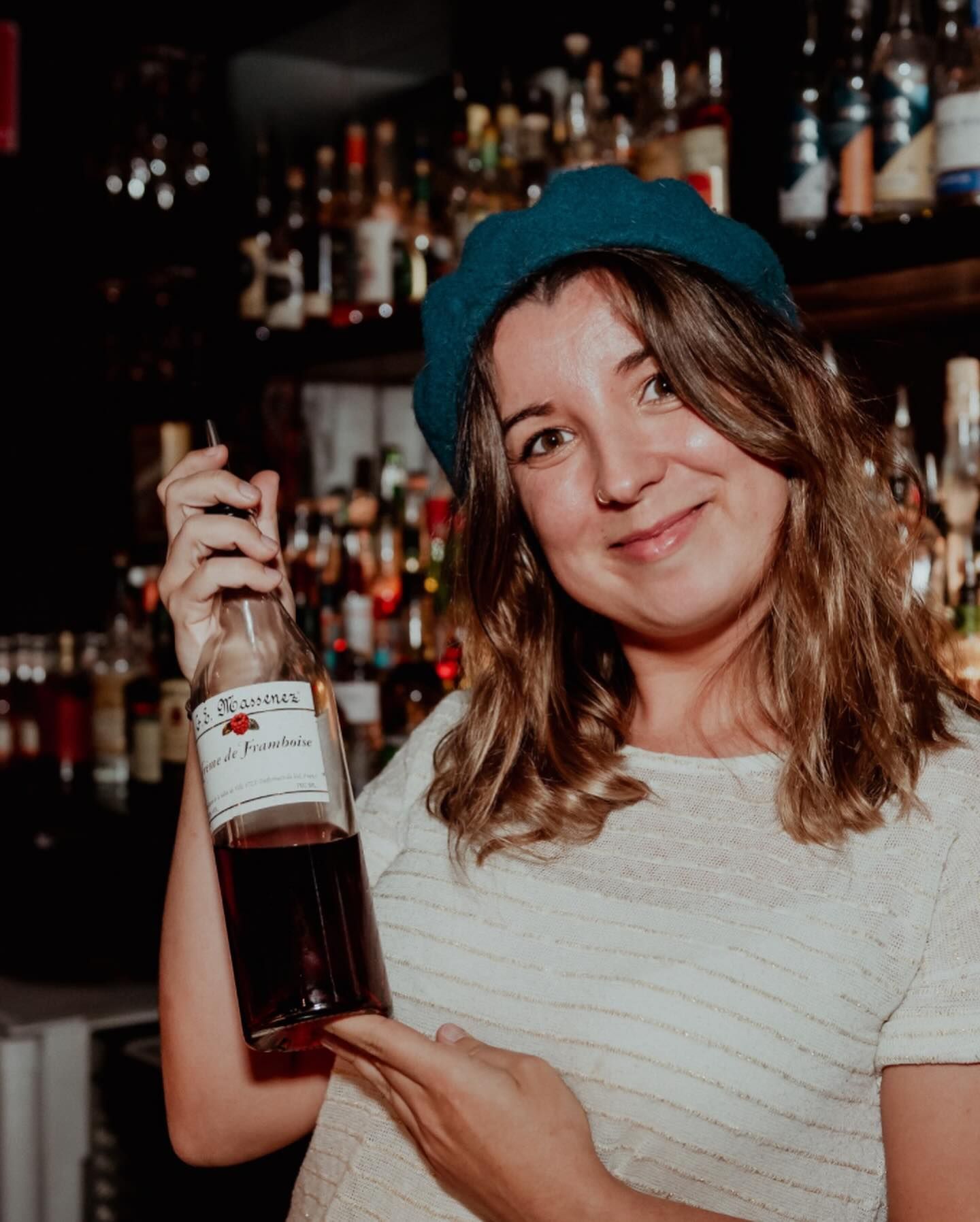 A woman in a blue hat is holding a bottle of wine.