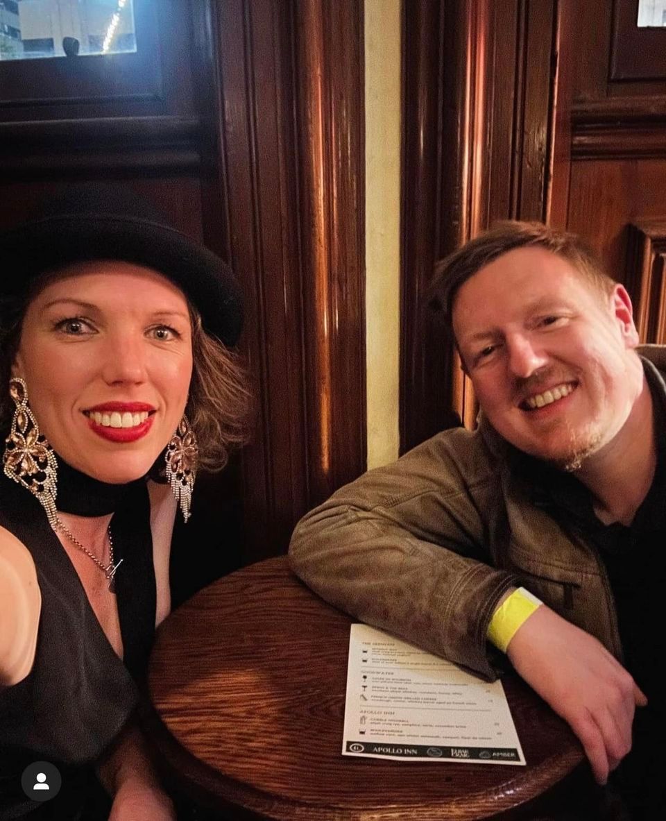 A man and a woman are posing for a picture while sitting at a table
