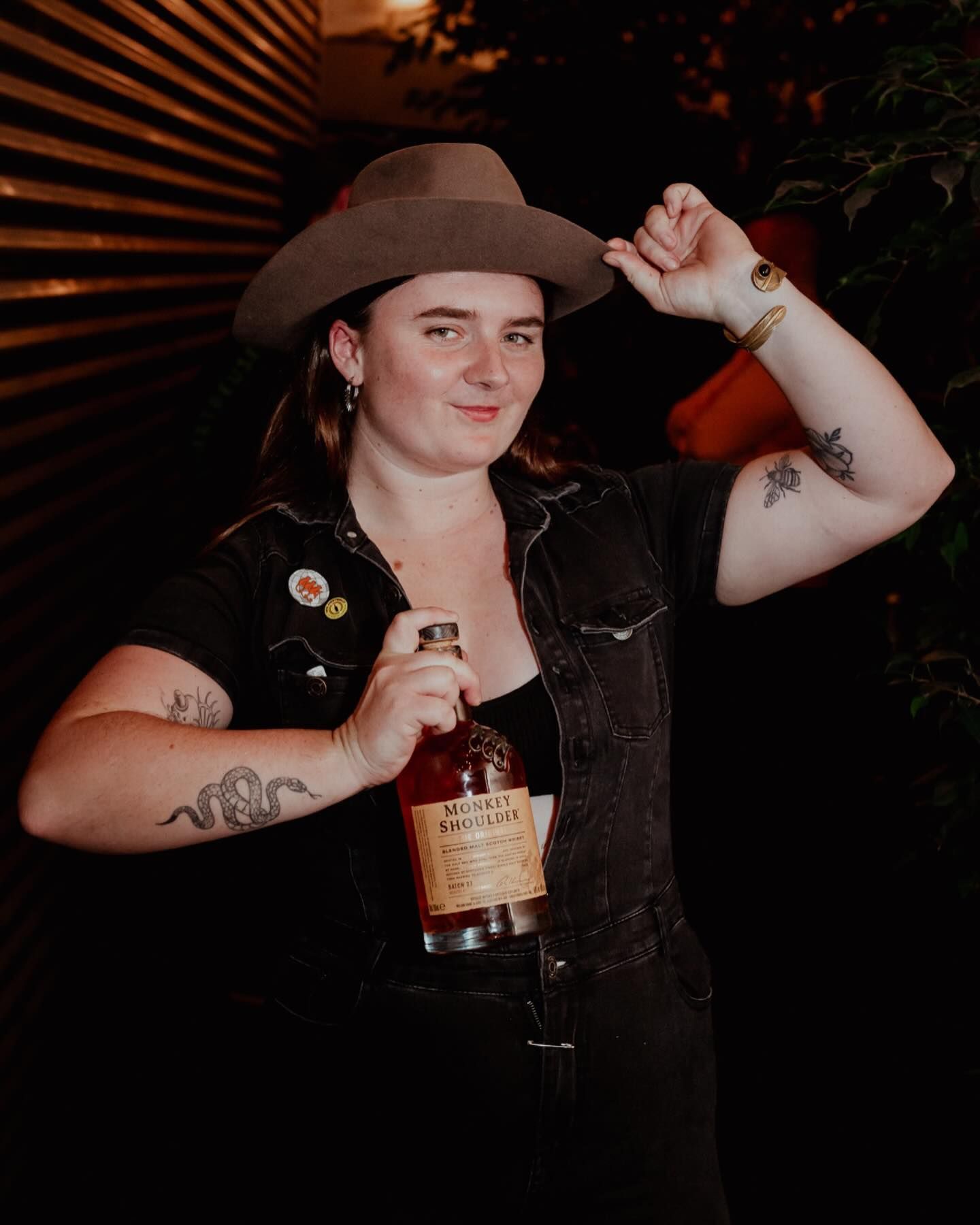 A woman in a cowboy hat is holding a bottle of whiskey.