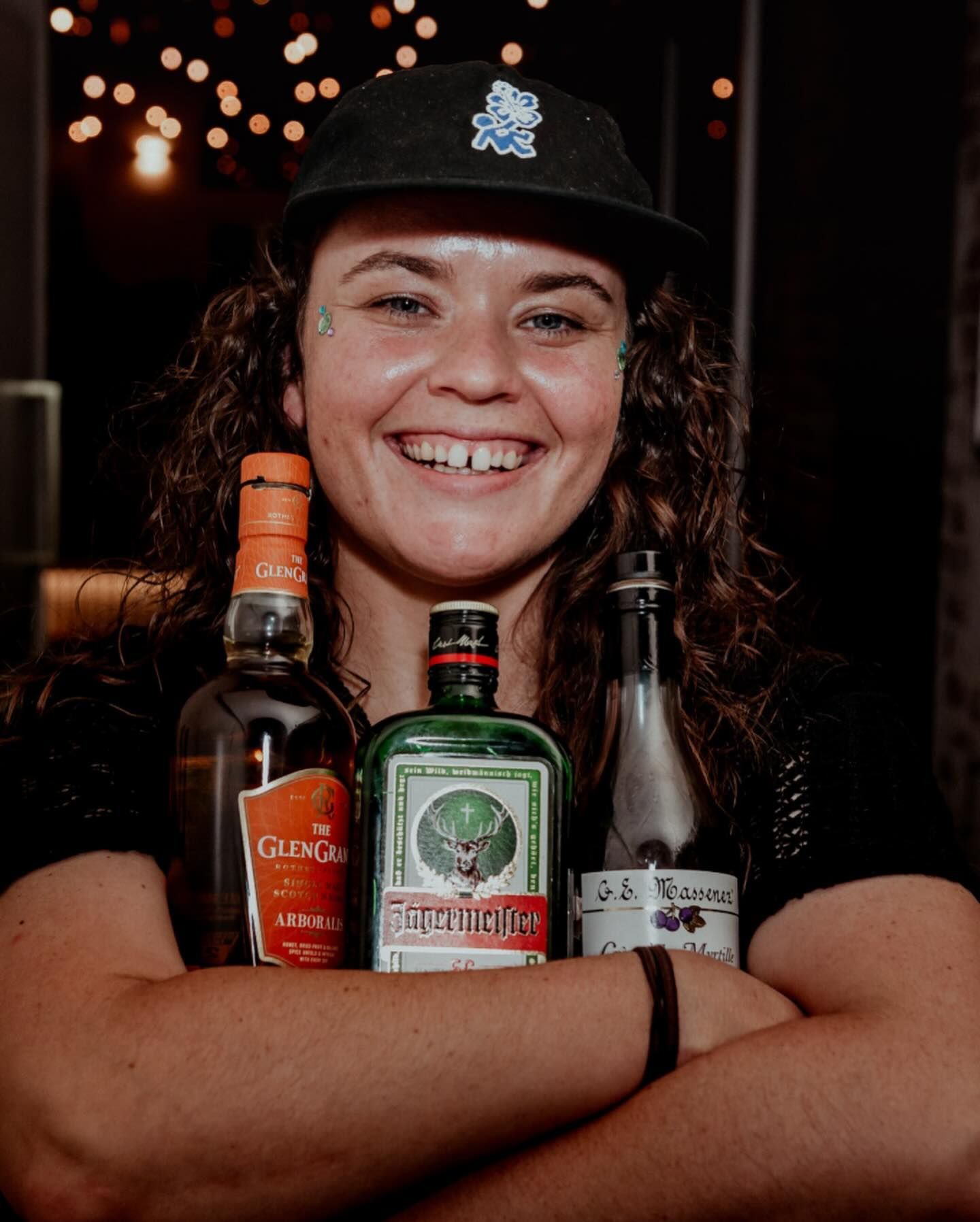 A woman wearing a hat is holding three bottles of alcohol.