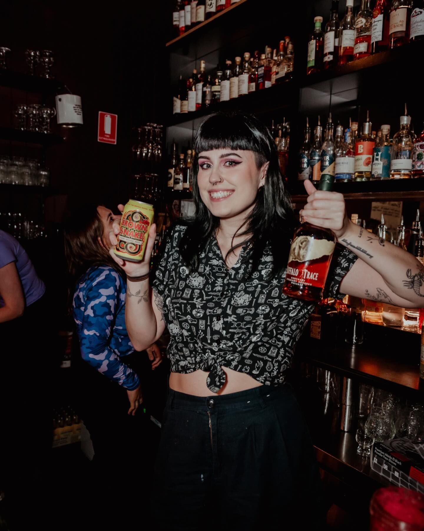 A woman is standing in Santé Cocktail Bar holding alcohol and giving a thumbs up.