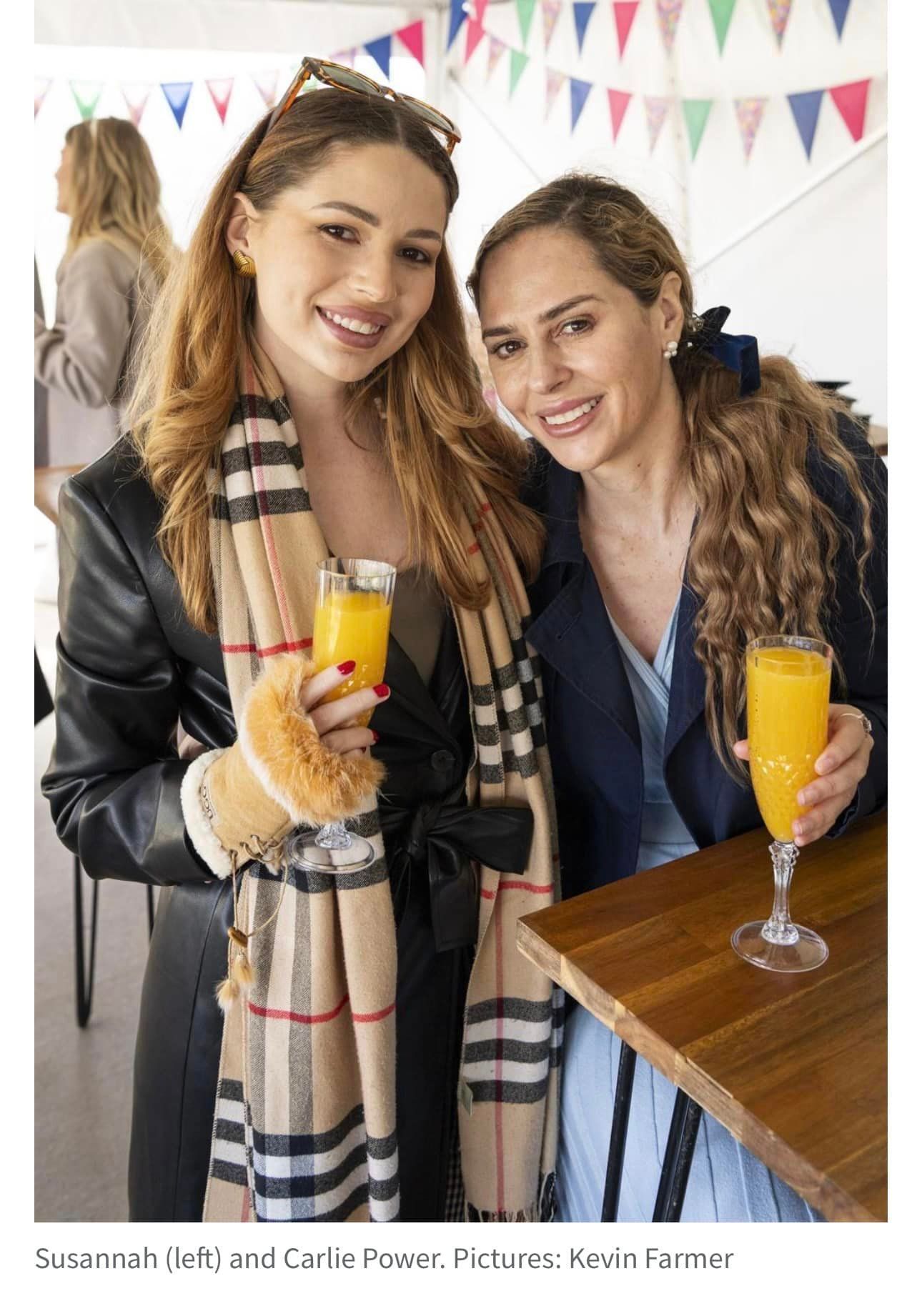 Two women are standing next to each other holding glasses of orange juice.