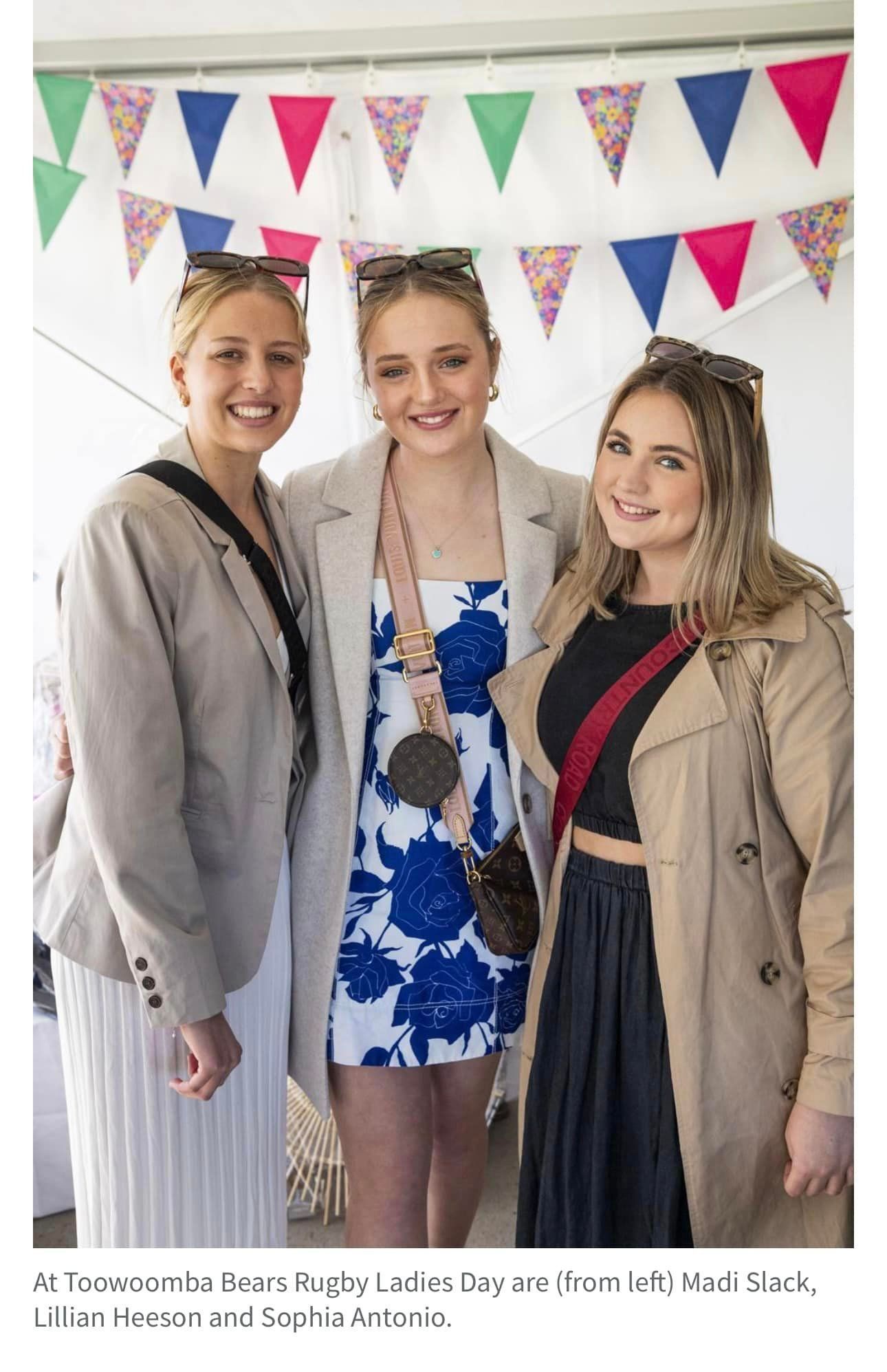 Three women are posing for a picture in front of a bunting.