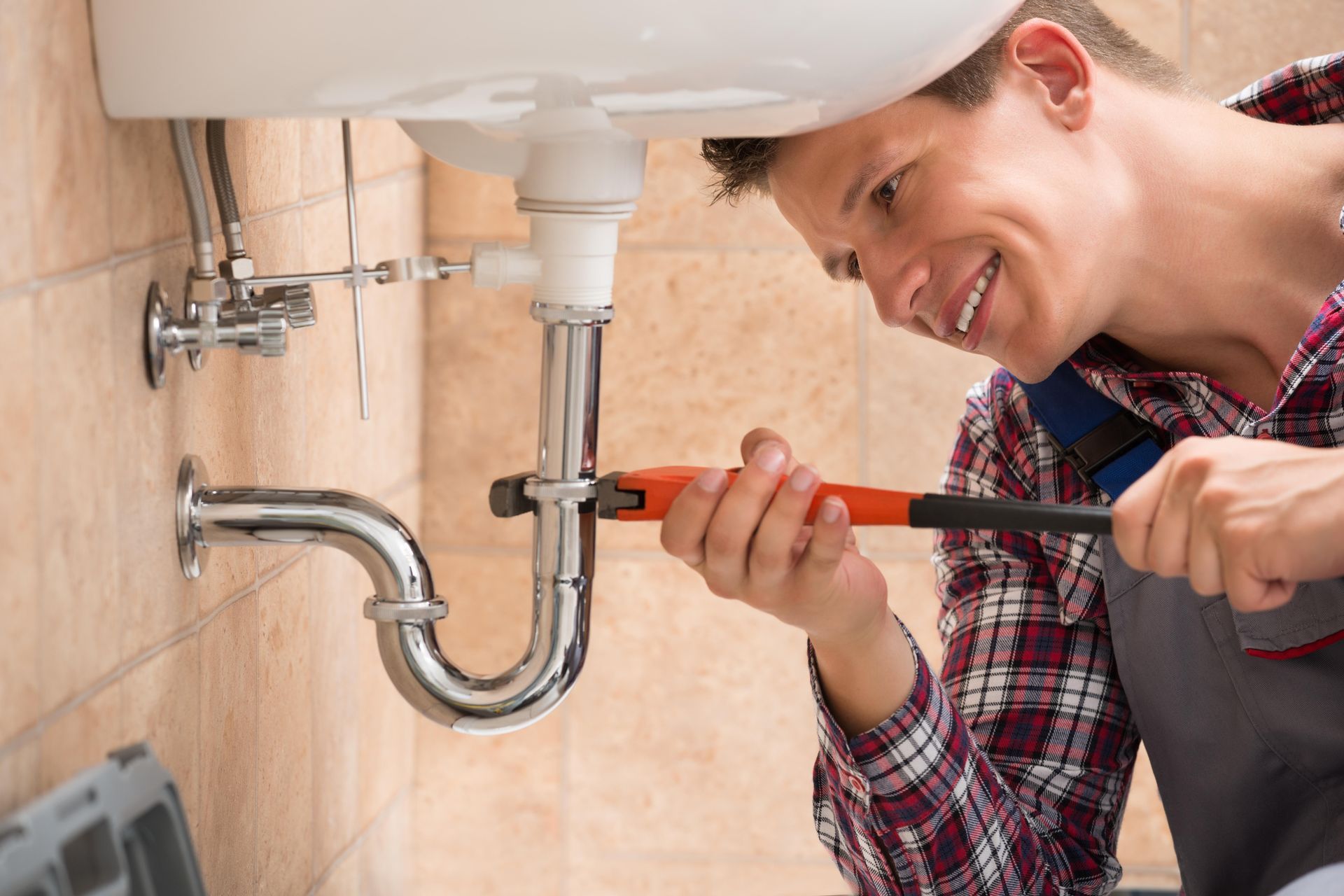 A plumber is fixing a sink pipe with a wrench.