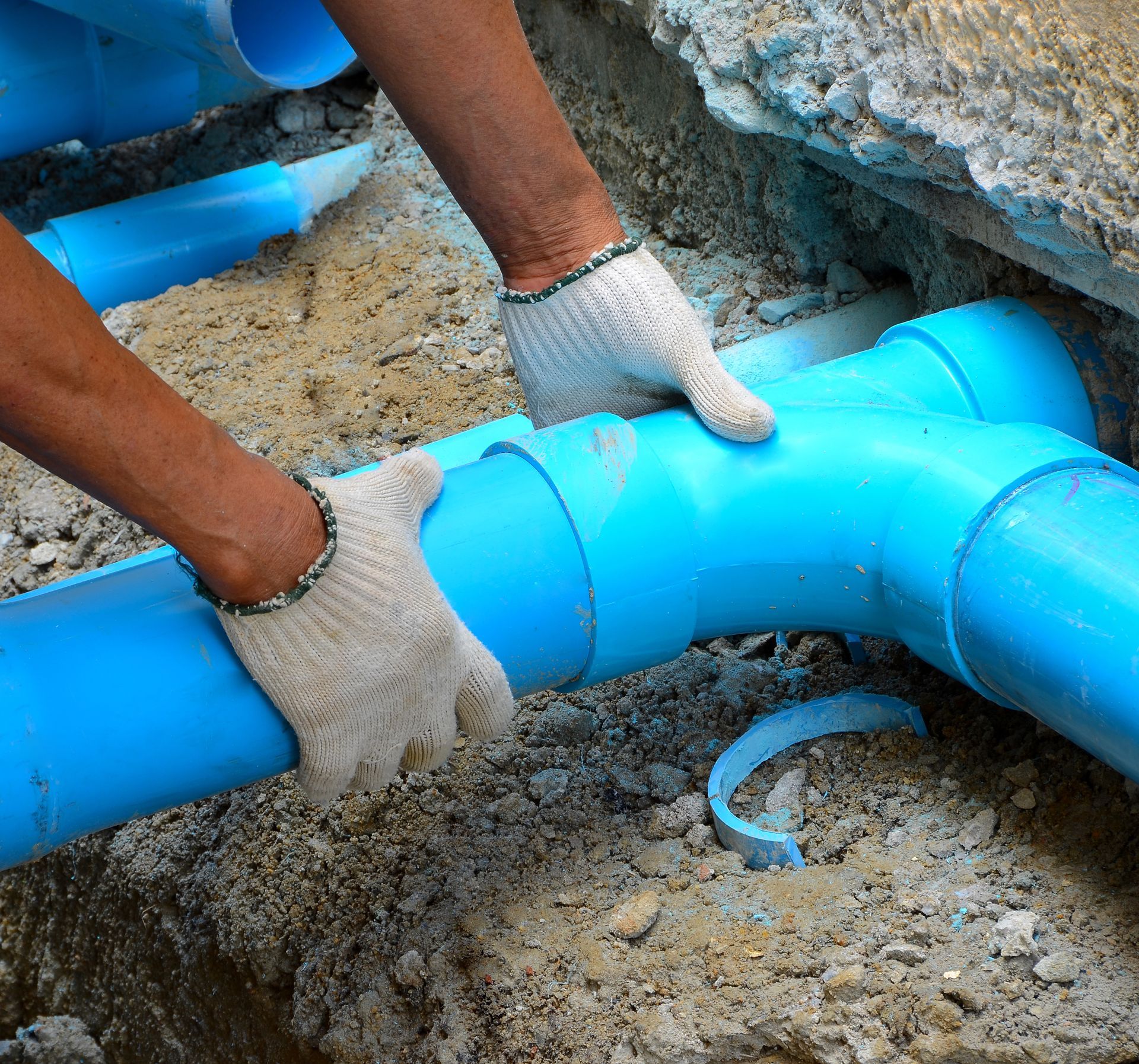 A person wearing gloves is working on a blue pipe