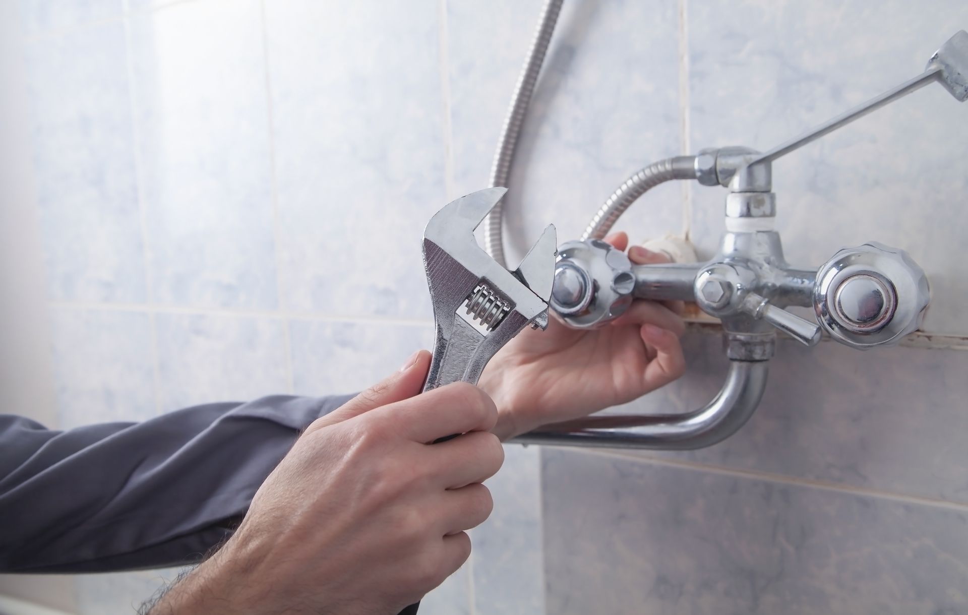 A man is fixing a faucet with a wrench in a bathroom.