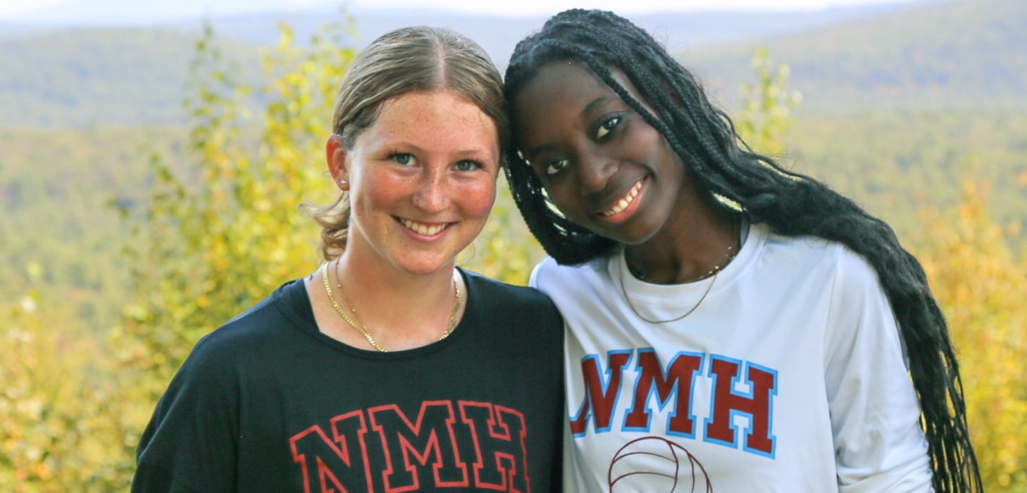 Two Montessori students smiling, outdoors with fall foliage in background.