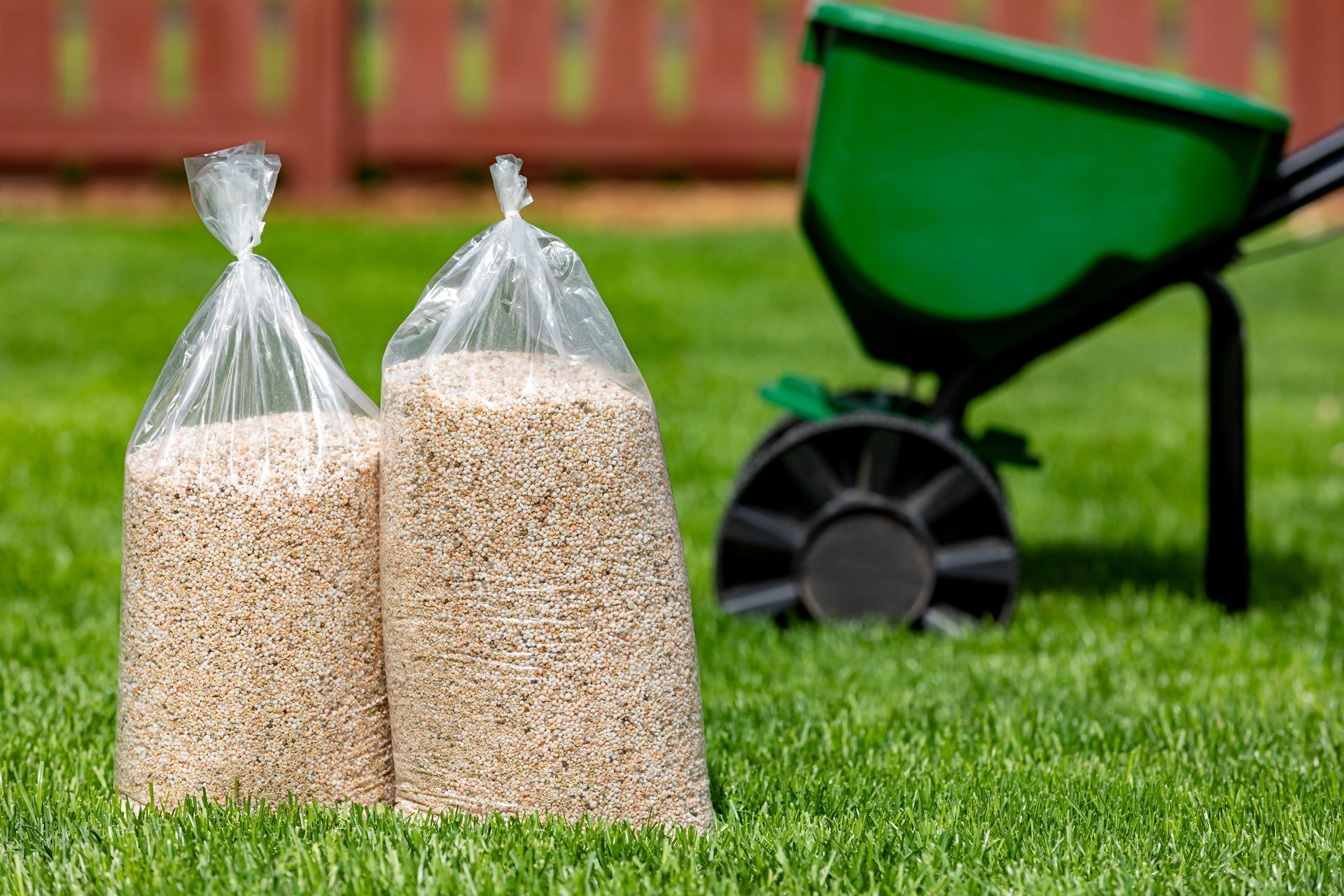 Two bags of lawn fertilizer with a broadcast spreader in a yard with healthy grass.