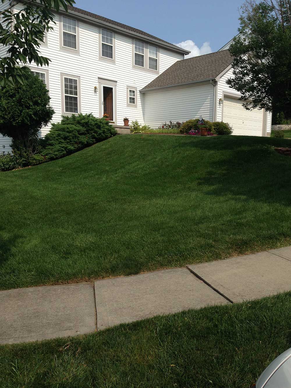 Two-story white house with a green lawn and a driveway on a sunny day.