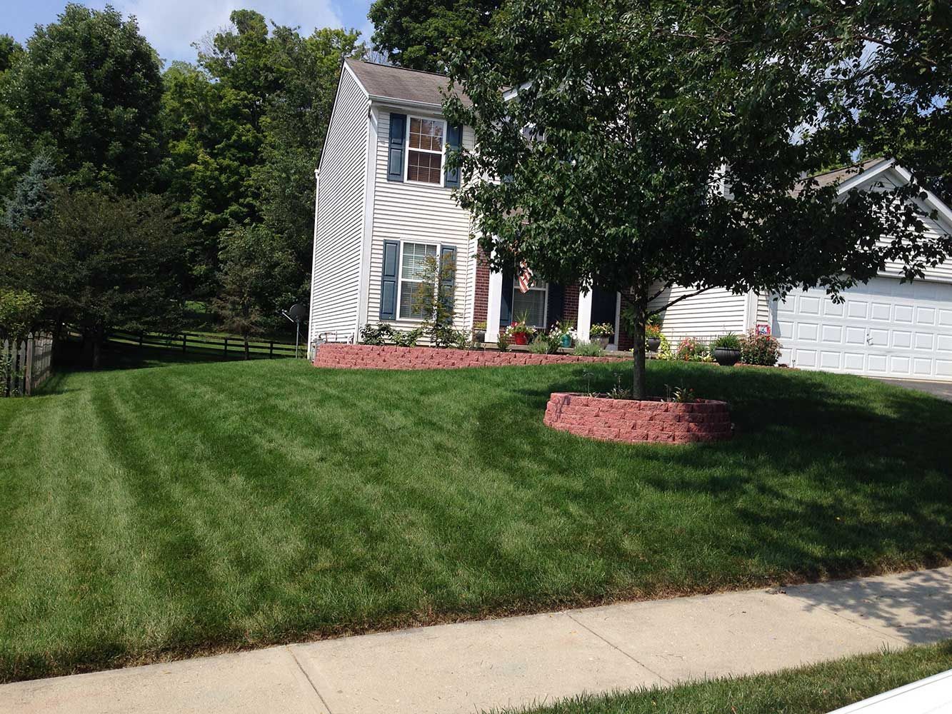 A two-story house with neatly mowed green lawn and a brick flowerbed.