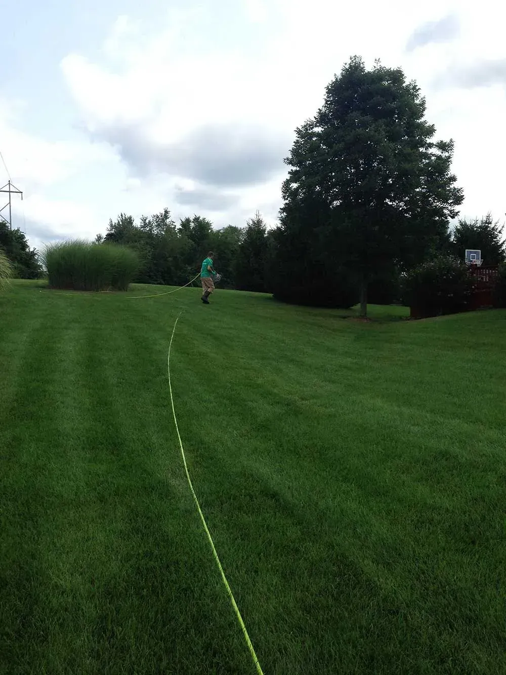 Person walking on green lawn with a yellow line, under a cloudy sky.