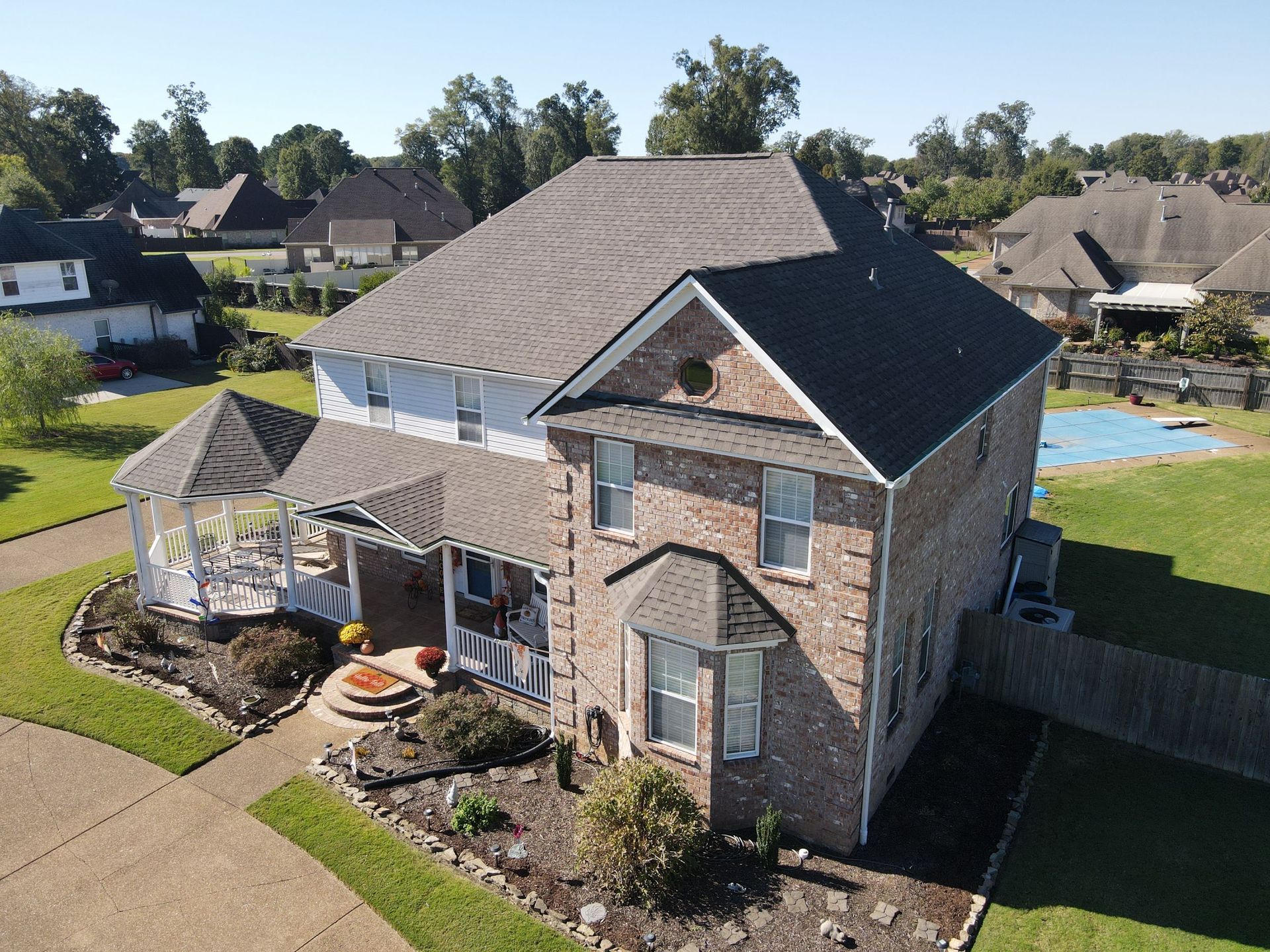 Aerial view of a brick two-story suburban house with a gazebo, patio, and landscaped yard.